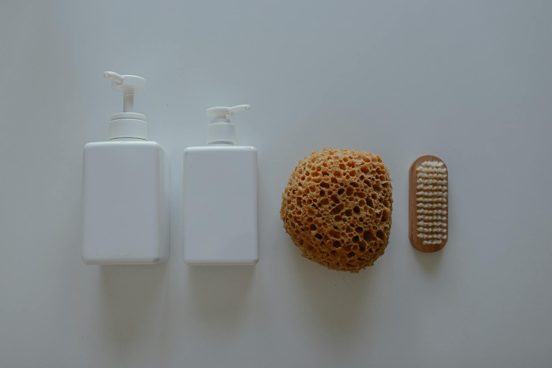 Flat lay of bath essentials including soap dispensers, a sponge, and a nail brush.