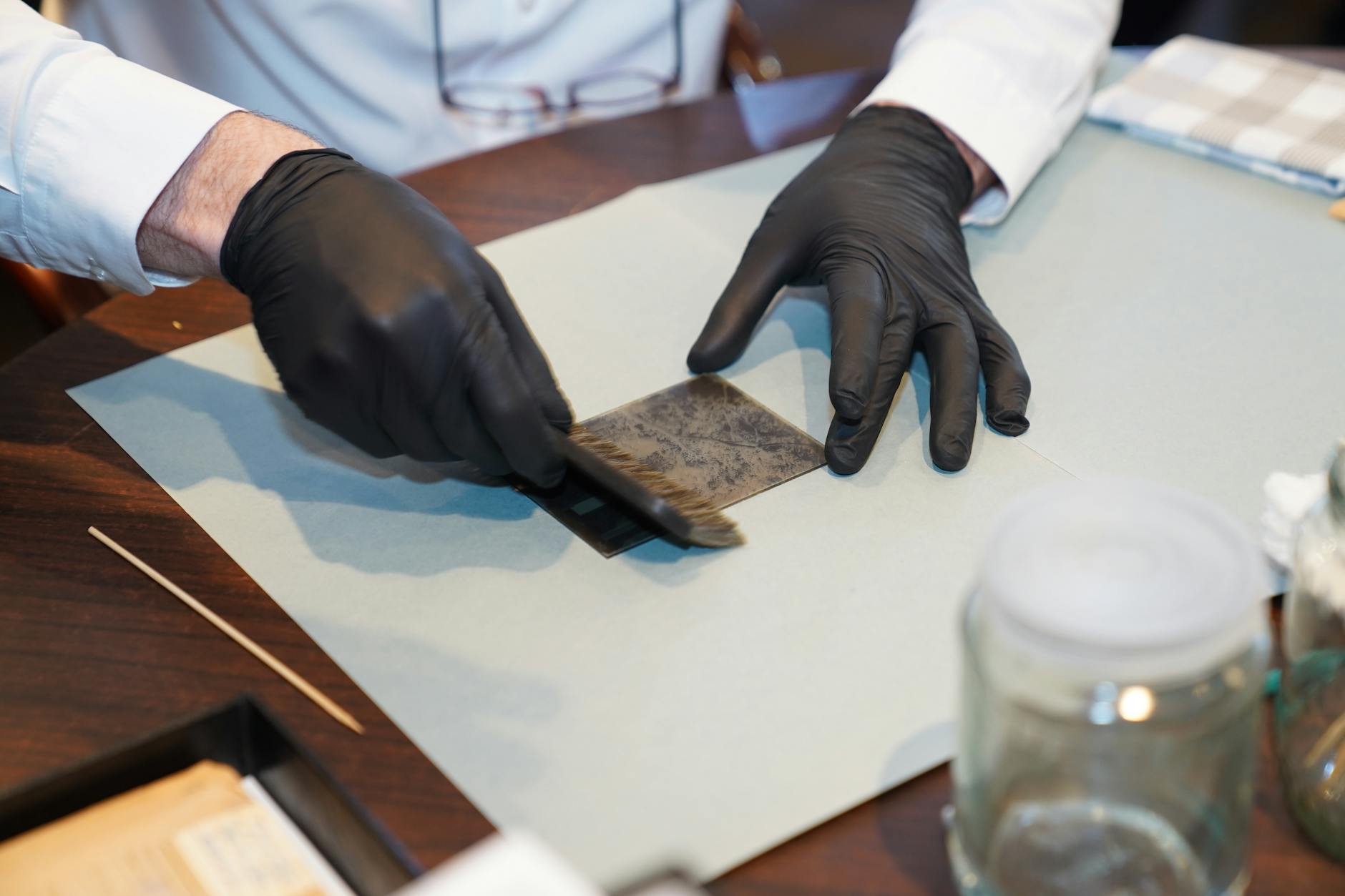 A restorer carefully working on a photograph with gloves and brush, focusing on details.