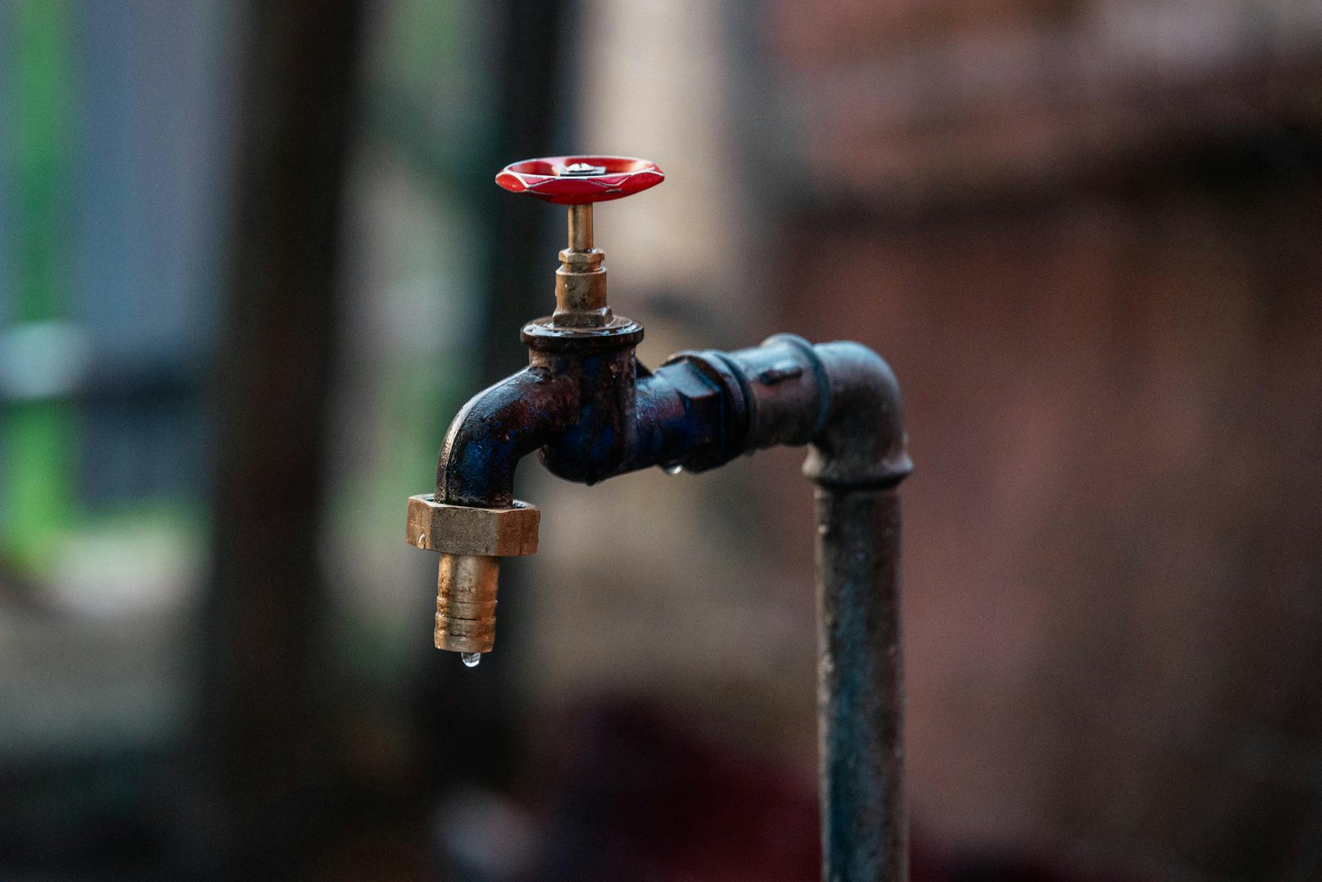 Close-up of a rusty outdoor water faucet with a single droplet falling from the spout.