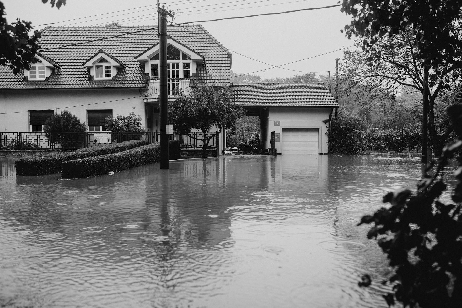 A flooded suburban house surrounded by high water, depicting severe weather impact.