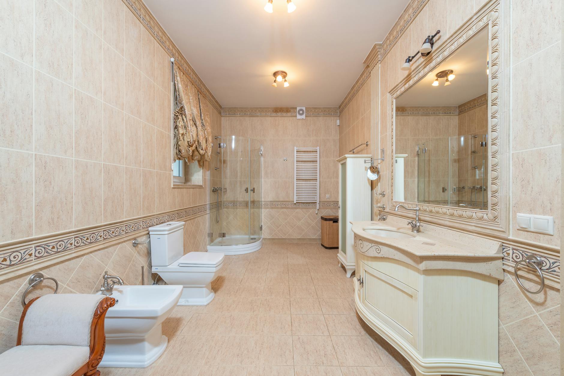 Spacious luxury bathroom featuring beige tiles, elegant furnishings, and modern fixtures.