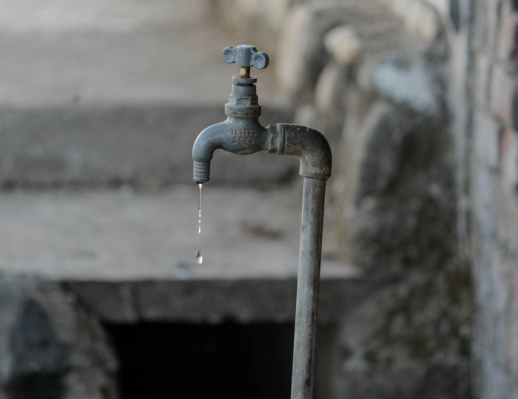 A close-up of a rustic outdoor faucet dripping water against a natural, textured background, symbolizing scarcity.
