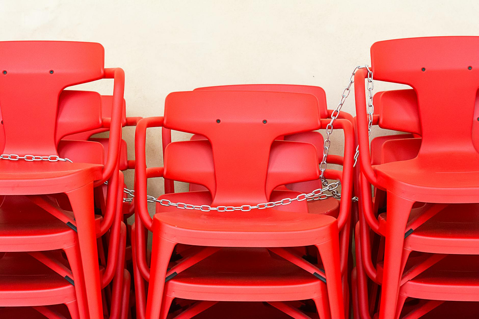 A stack of red plastic chairs secured with chains against a neutral background.