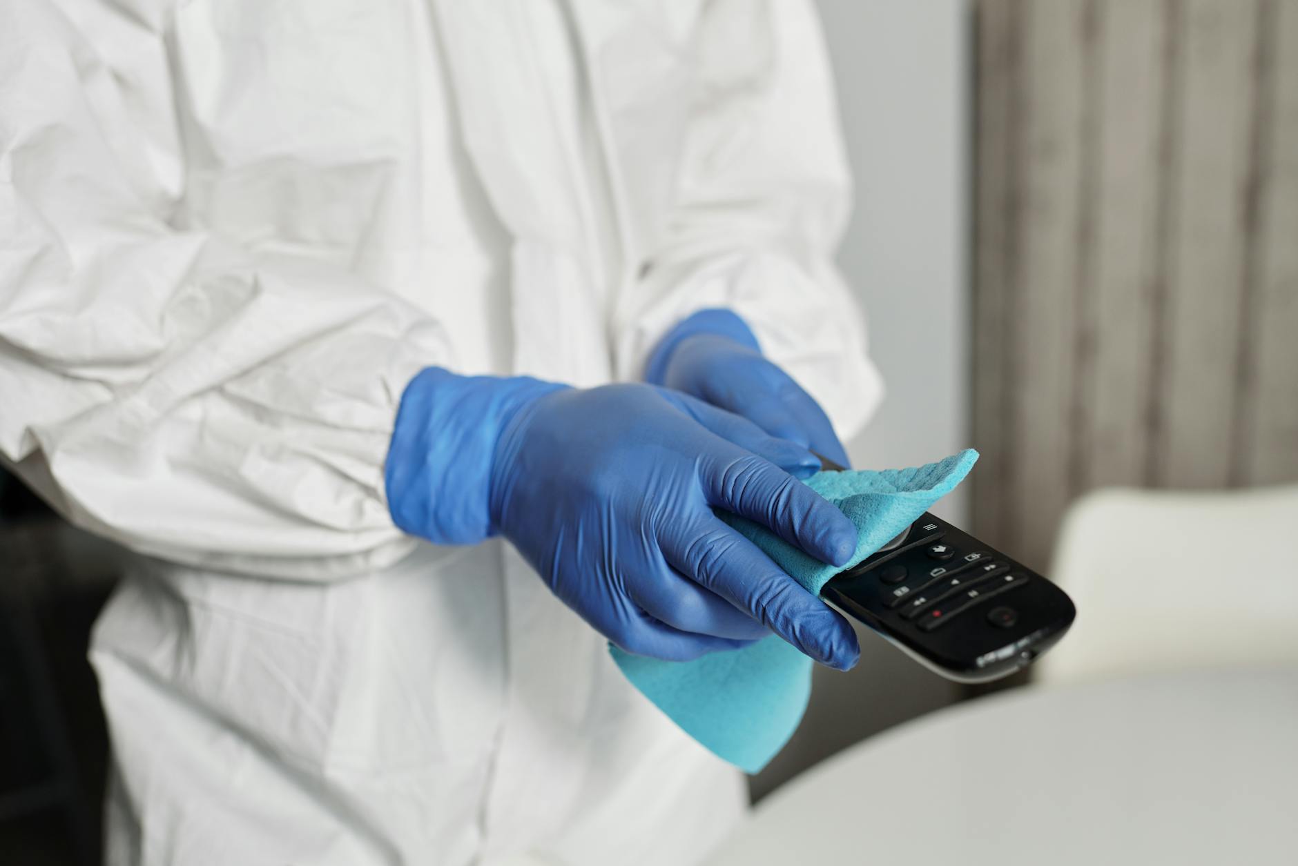 Close-up of a person disinfecting a remote control wearing protective gloves, ensuring cleanliness.