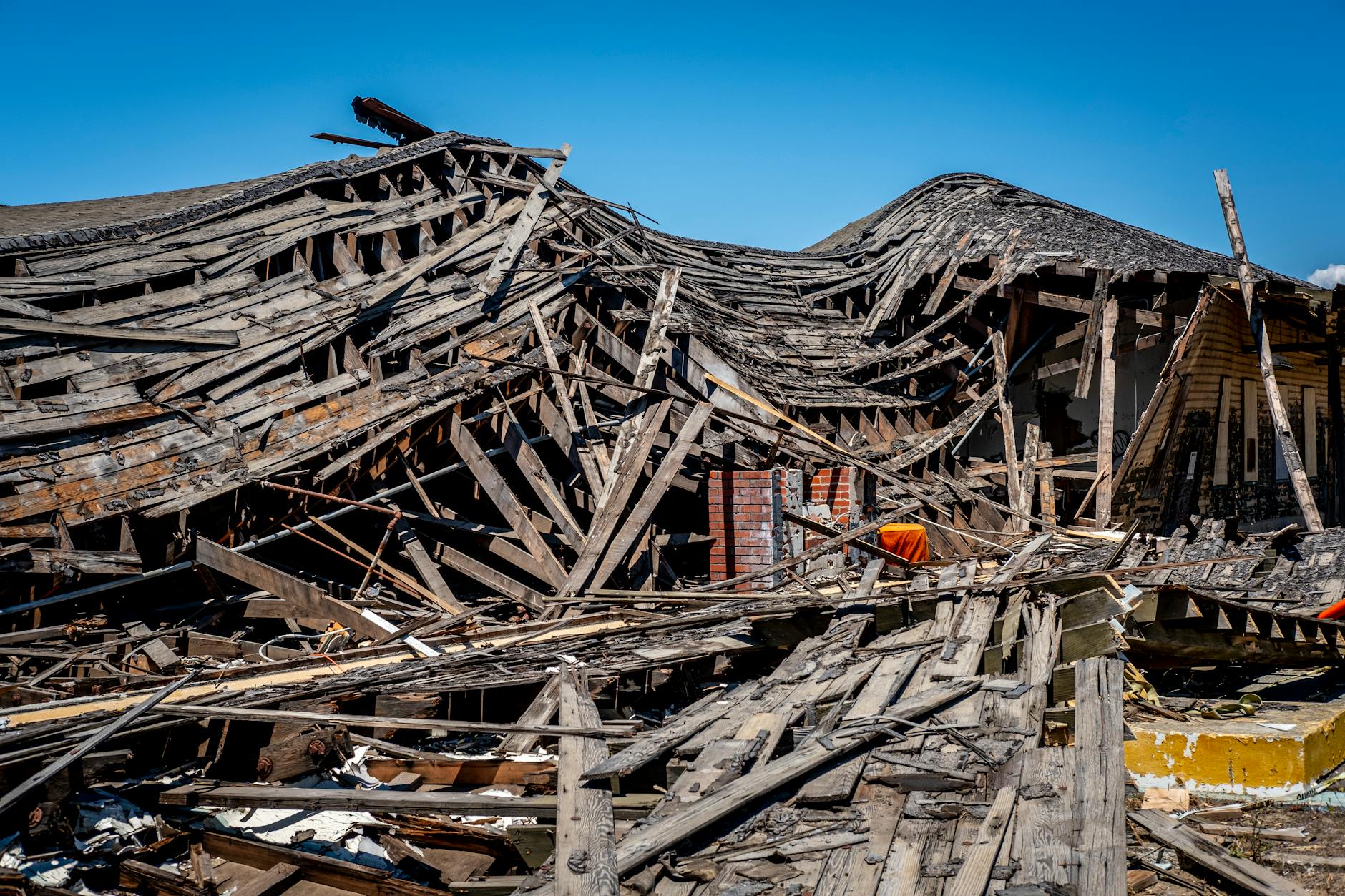 A dramatic view of a destroyed wooden building after a catastrophe, showing debris and structural failure.