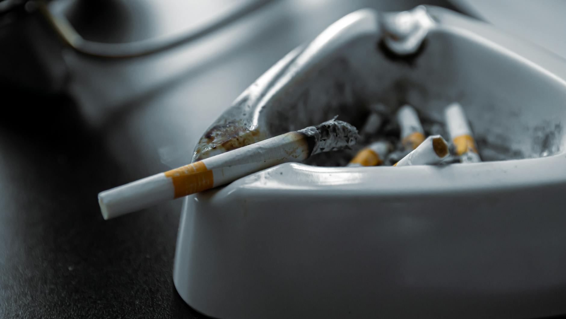 A close-up shot of a white ashtray filled with used cigarettes on a dark surface.