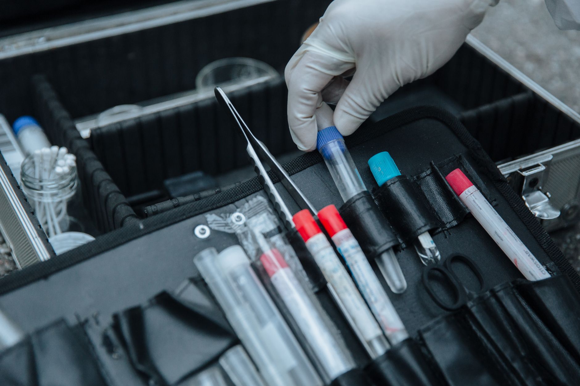 Gloved hand handling test tube in forensic equipment case at crime scene.