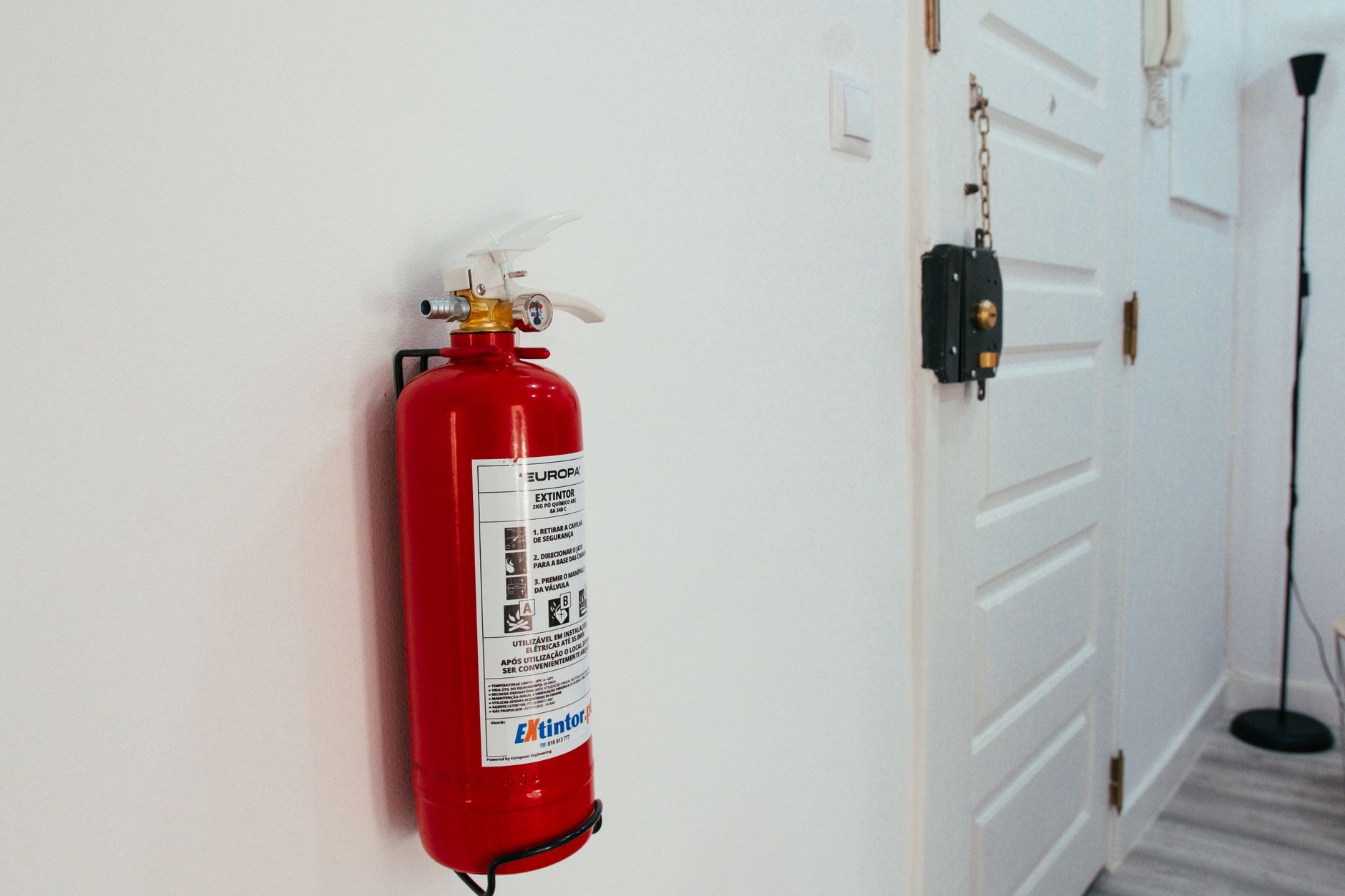 Red fire extinguisher mounted on a white wall in a modern apartment hallway.