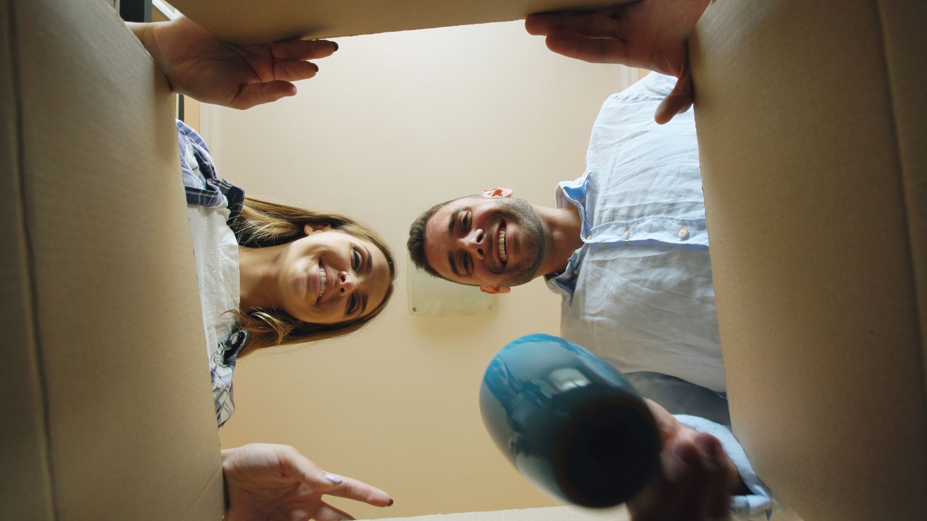 Smiling couple unpacking a cardboard box, symbolizing moving into a new home.