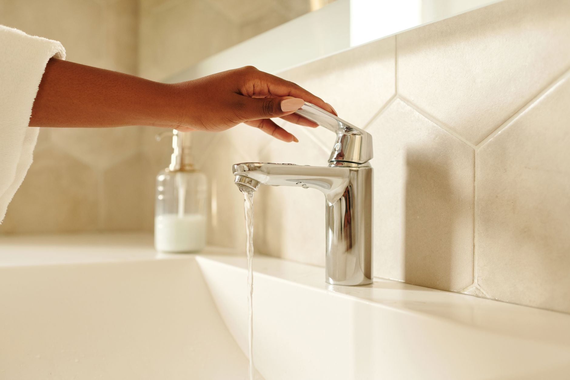 A close-up shot of a hand operating a chrome bathroom faucet with water flowing in a modern bathroom setting.