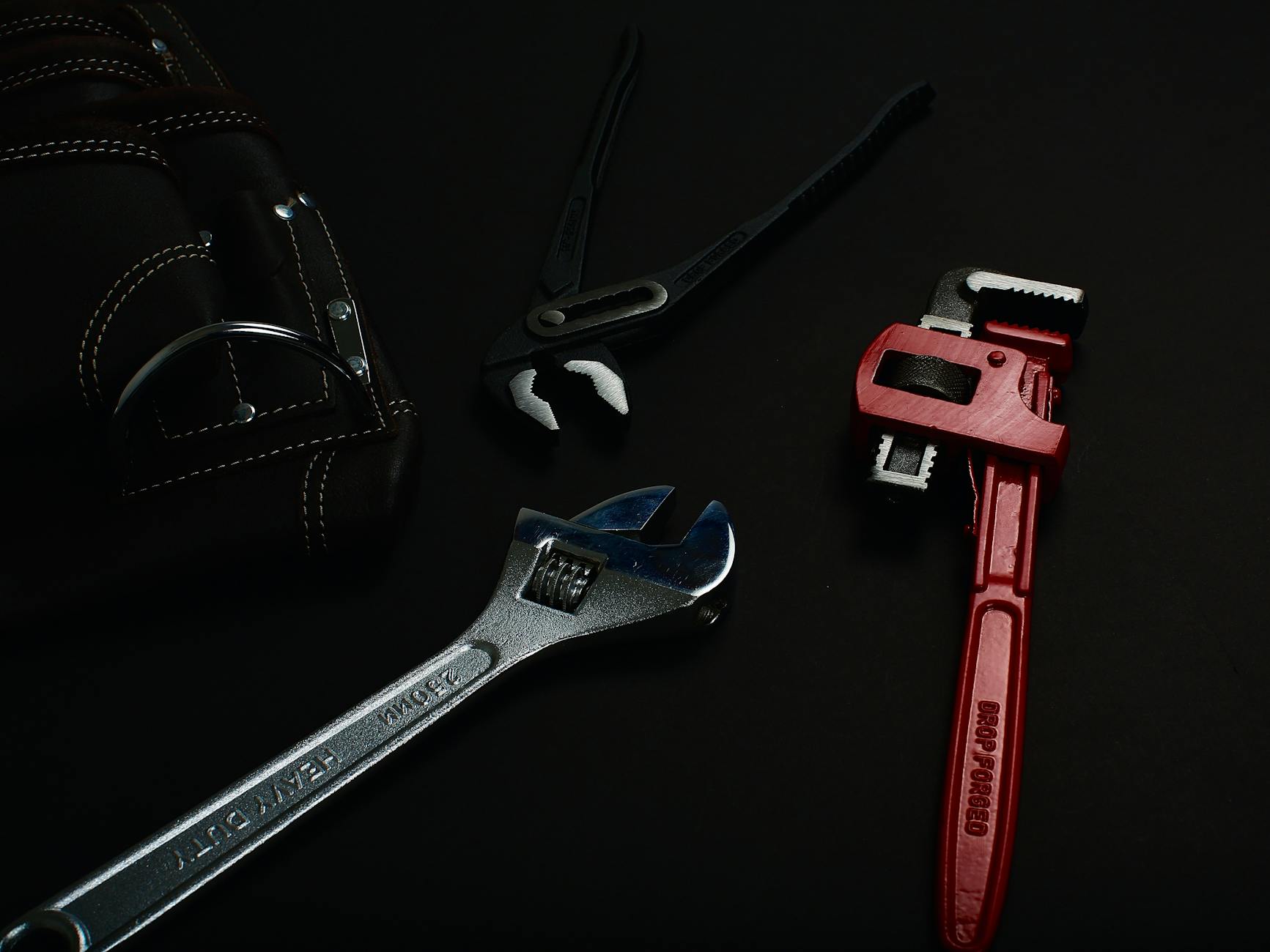 Close-up of various hand tools including wrenches and pliers on a dark surface.