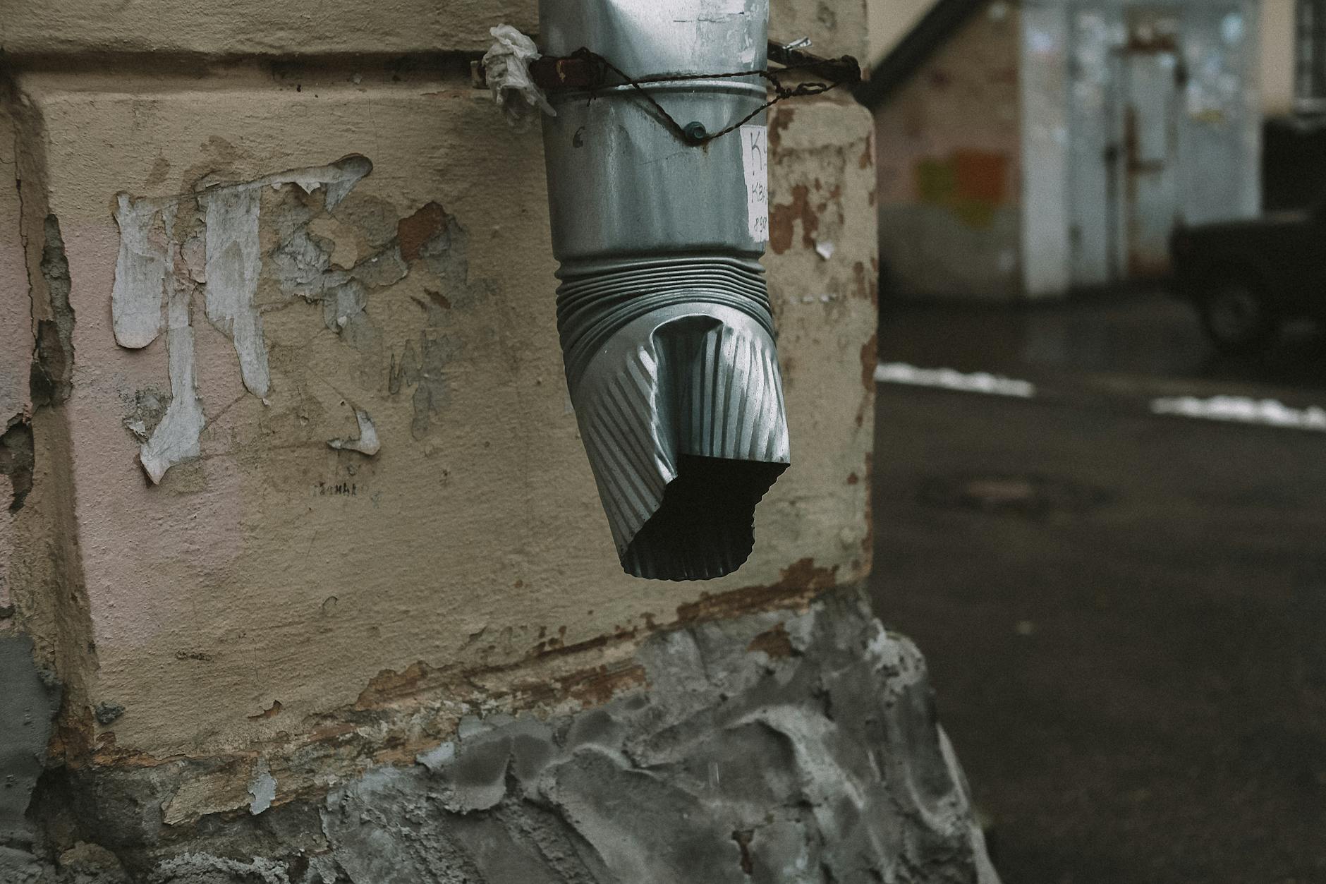 A metal drainage pipe with a rustic appearance on an aged wall with flaking paint.