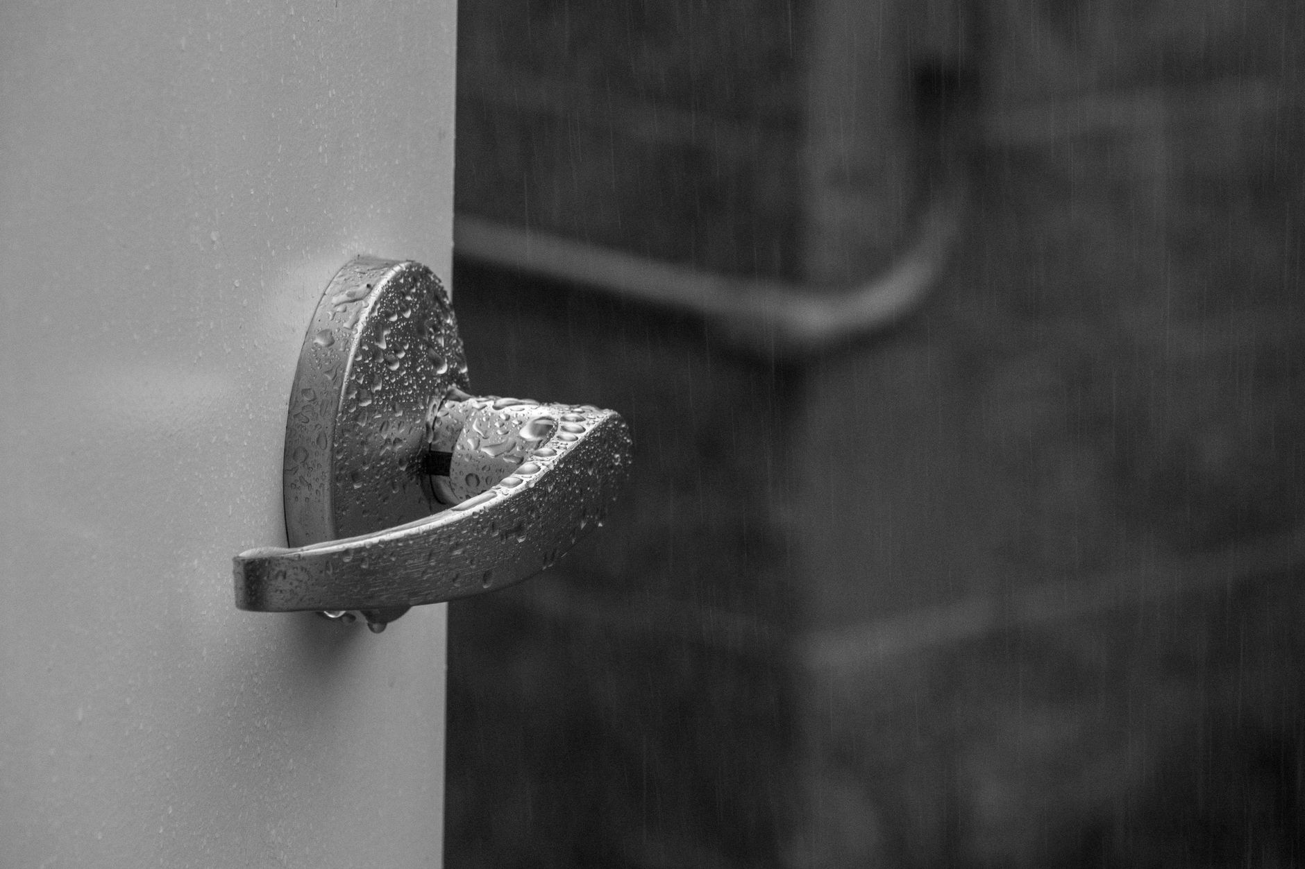 Black and white photo capturing a wet door handle outdoors in rainy weather.