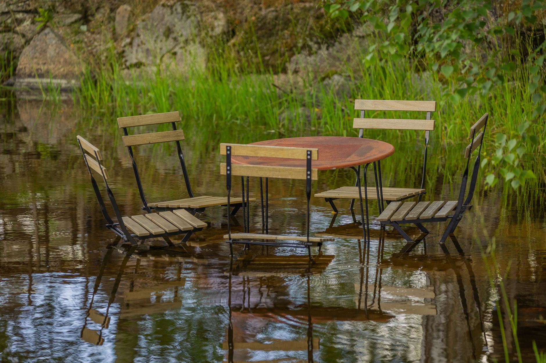 A unique scene of a wooden table and chairs partially submerged in a natural water setting.
