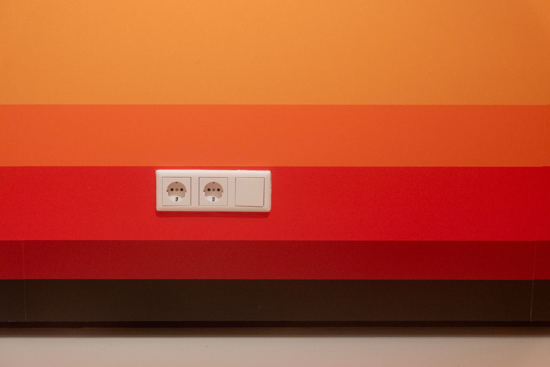 Minimalist design of orange and red striped wall with dual sockets.