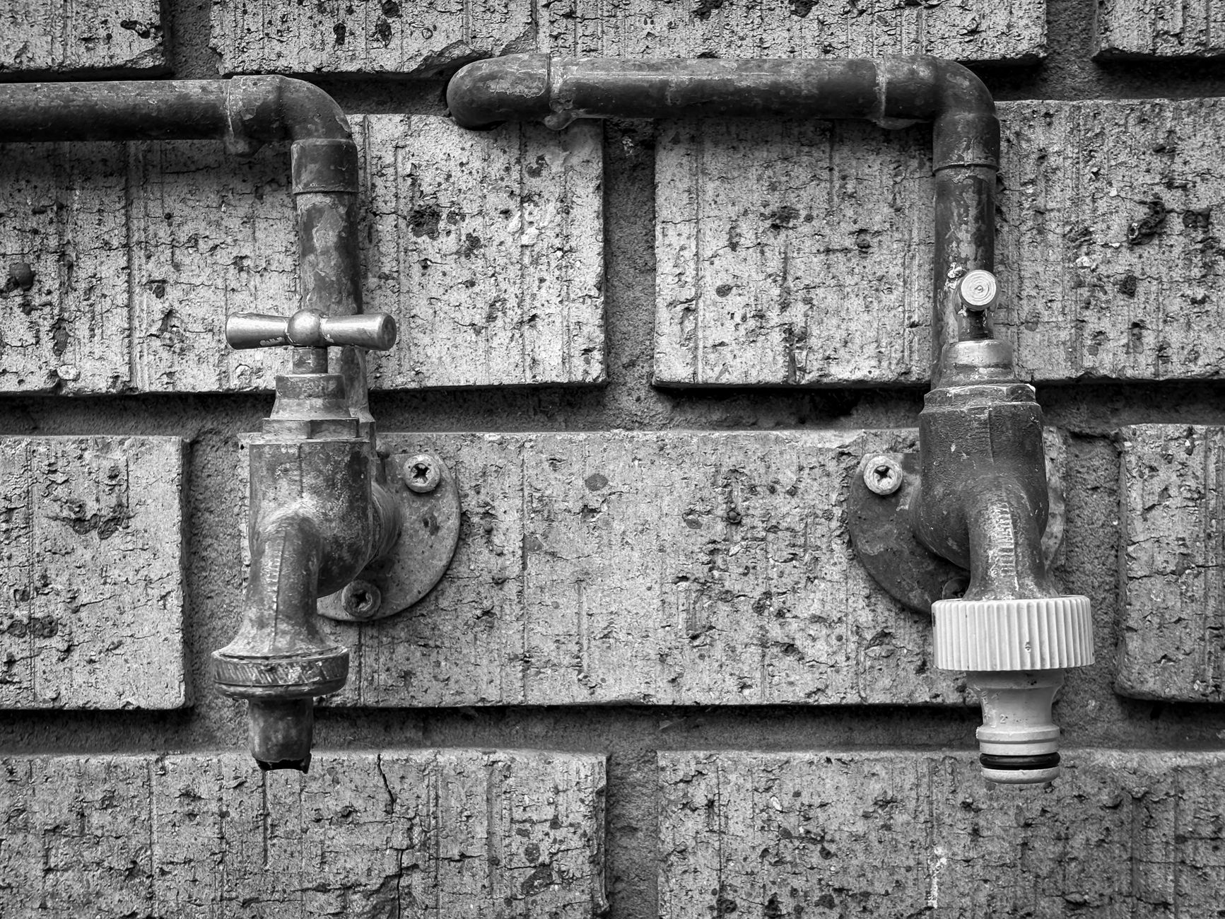 Close-up of vintage outdoor plumbing taps on a brick wall, black and white.