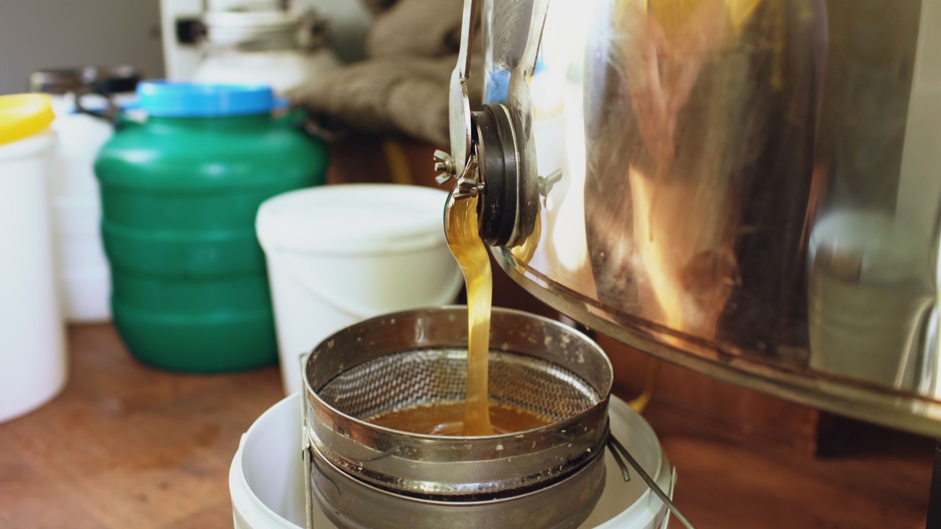 Honey flowing from a large stainless steel extractor into a filter in a beekeeping setup.
