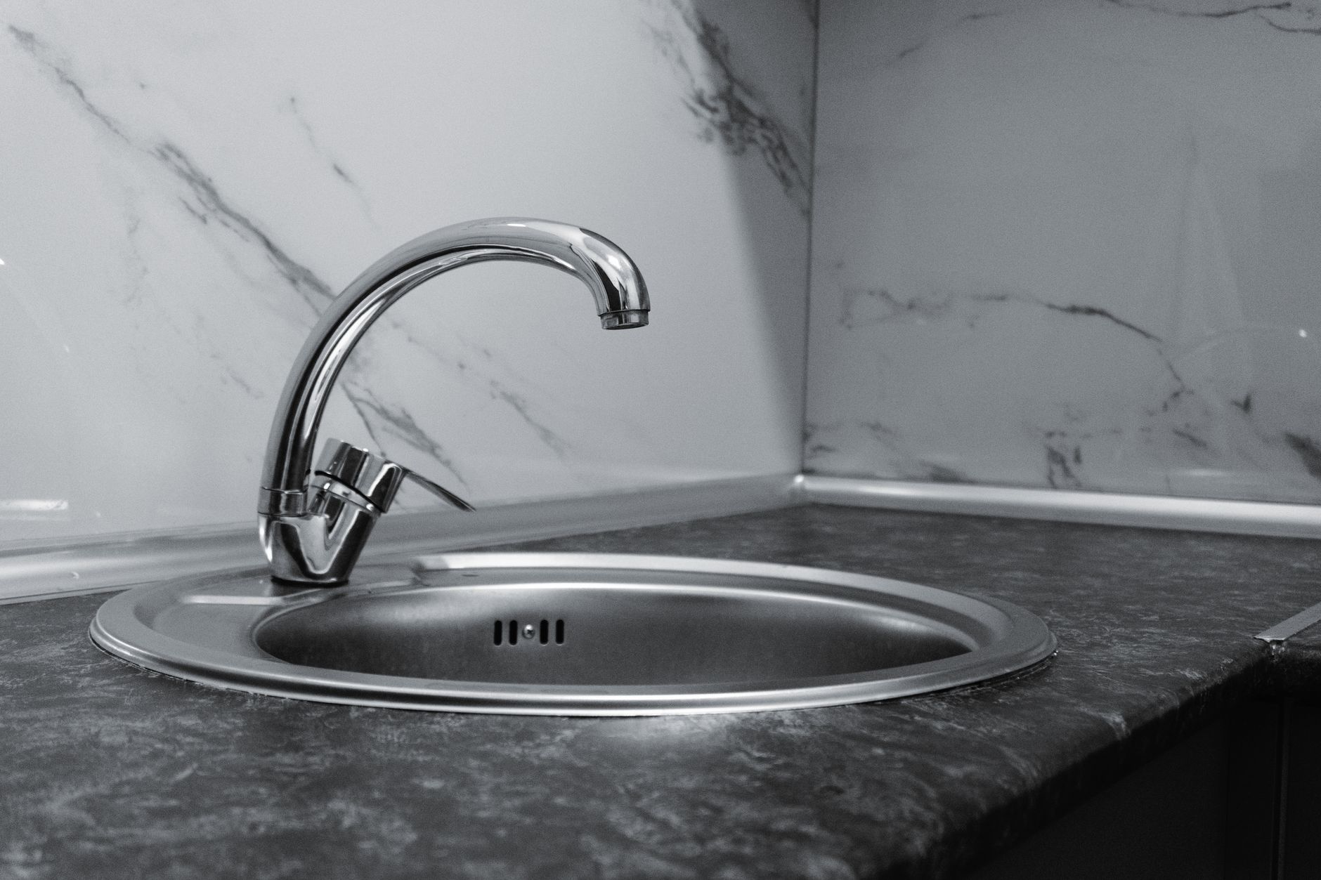 Stainless steel kitchen sink and faucet against marble backsplash in a modern kitchen.