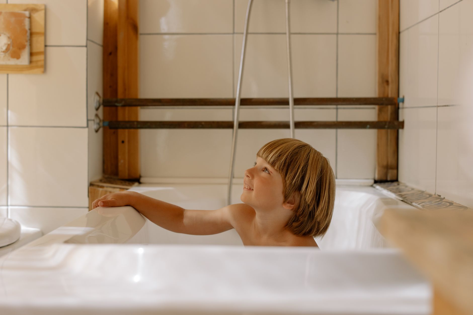 A young boy smiles in a modern, cozy bathroom characterized by warm wooden elements.