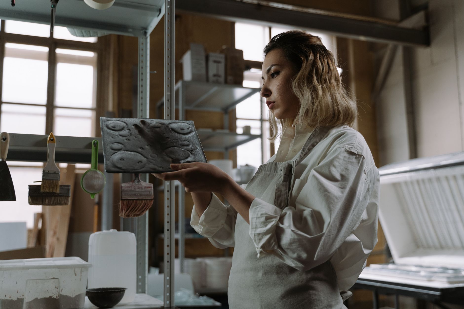 Craftswoman in apron examining ceramic molds in workshop, highlighting artistry and focus.