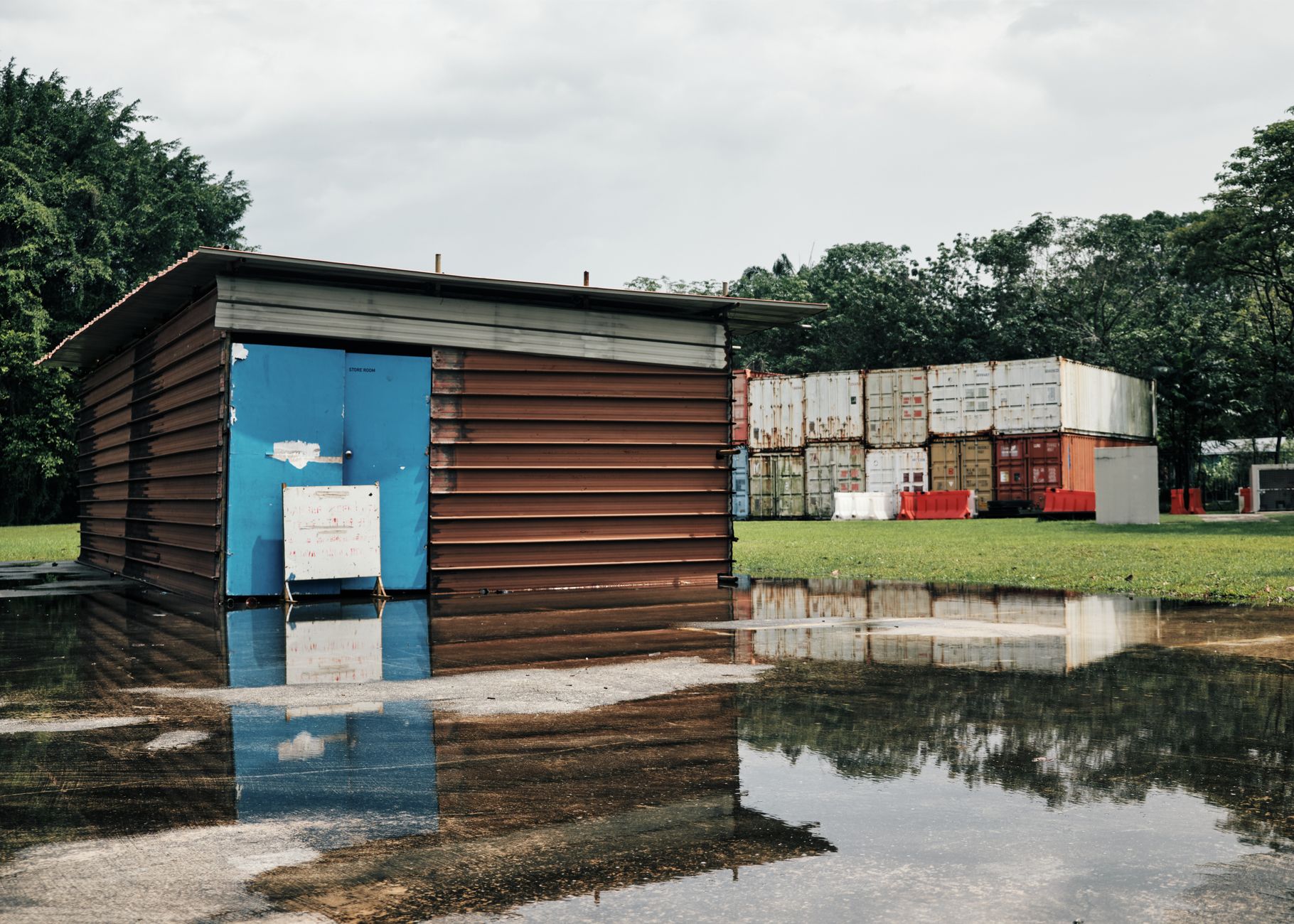 A shed and shipping containers reflected in water on an overcast day