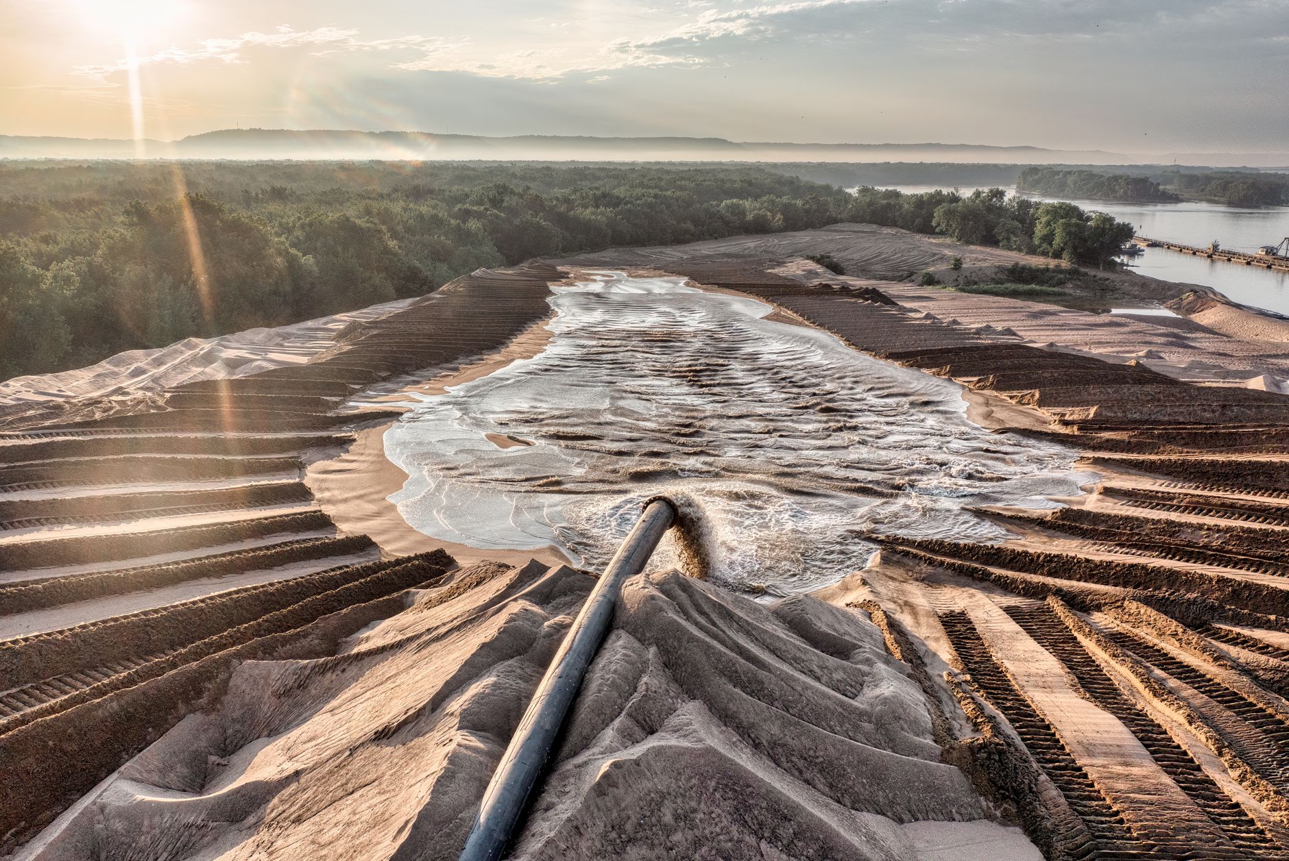 Drone shot of sand processing with flowing water and forest backdrop in Reads Landing, MN, at sunset.