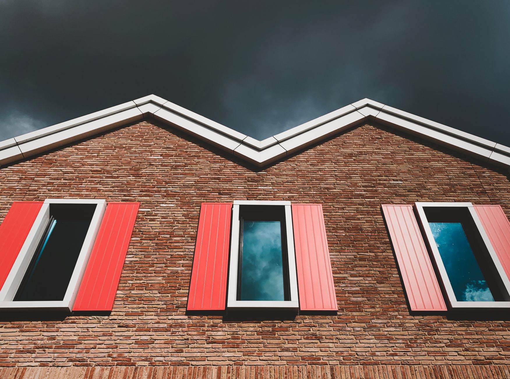 Low angle view of red brick facade with red shutters under a dramatic sky in Halfweg, Netherlands.