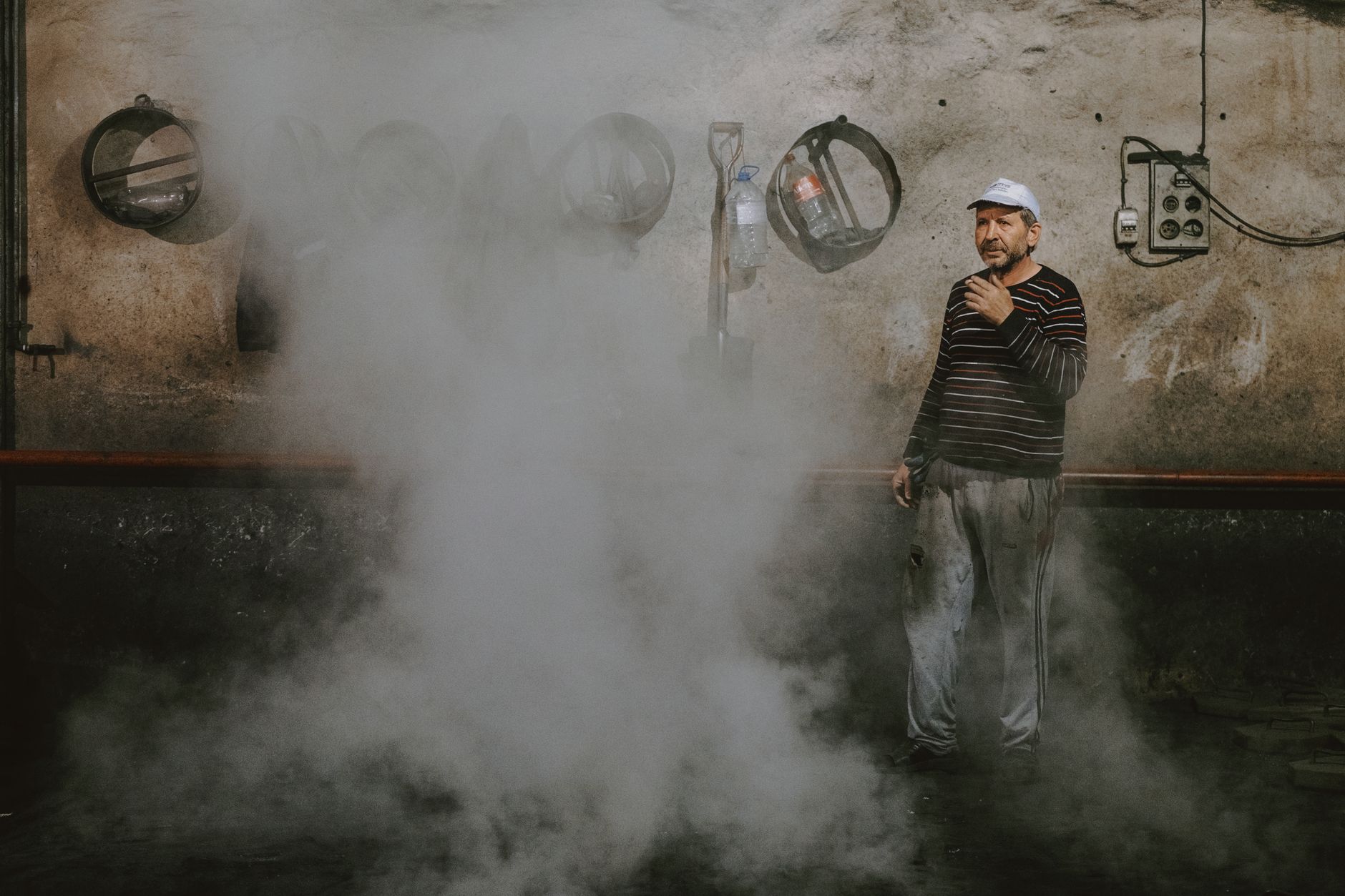 Man standing in a smoky industrial setting, exuding a gritty and authentic atmosphere.