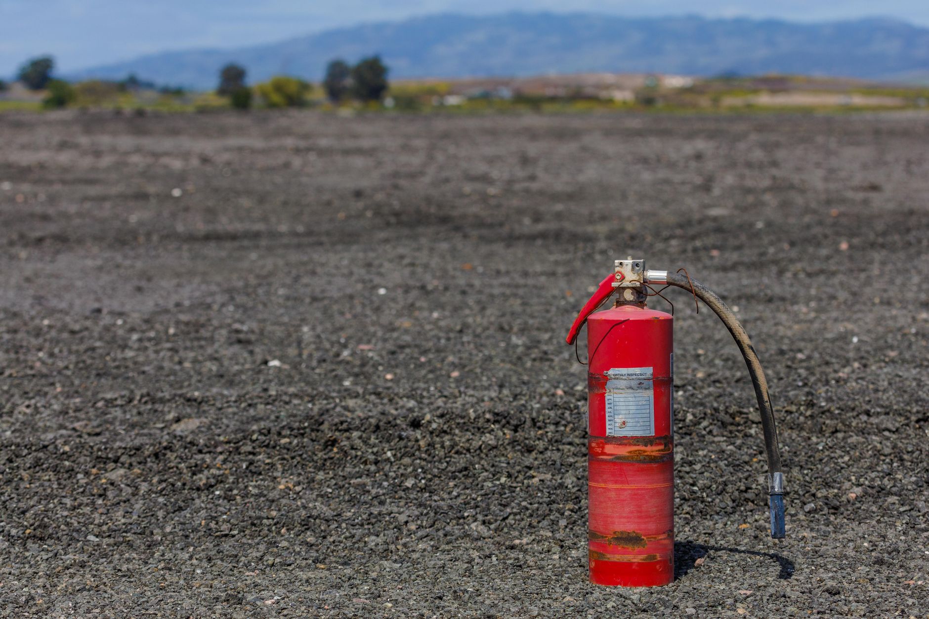A solitary rusty fire extinguisher stands on a barren gravel landscape.