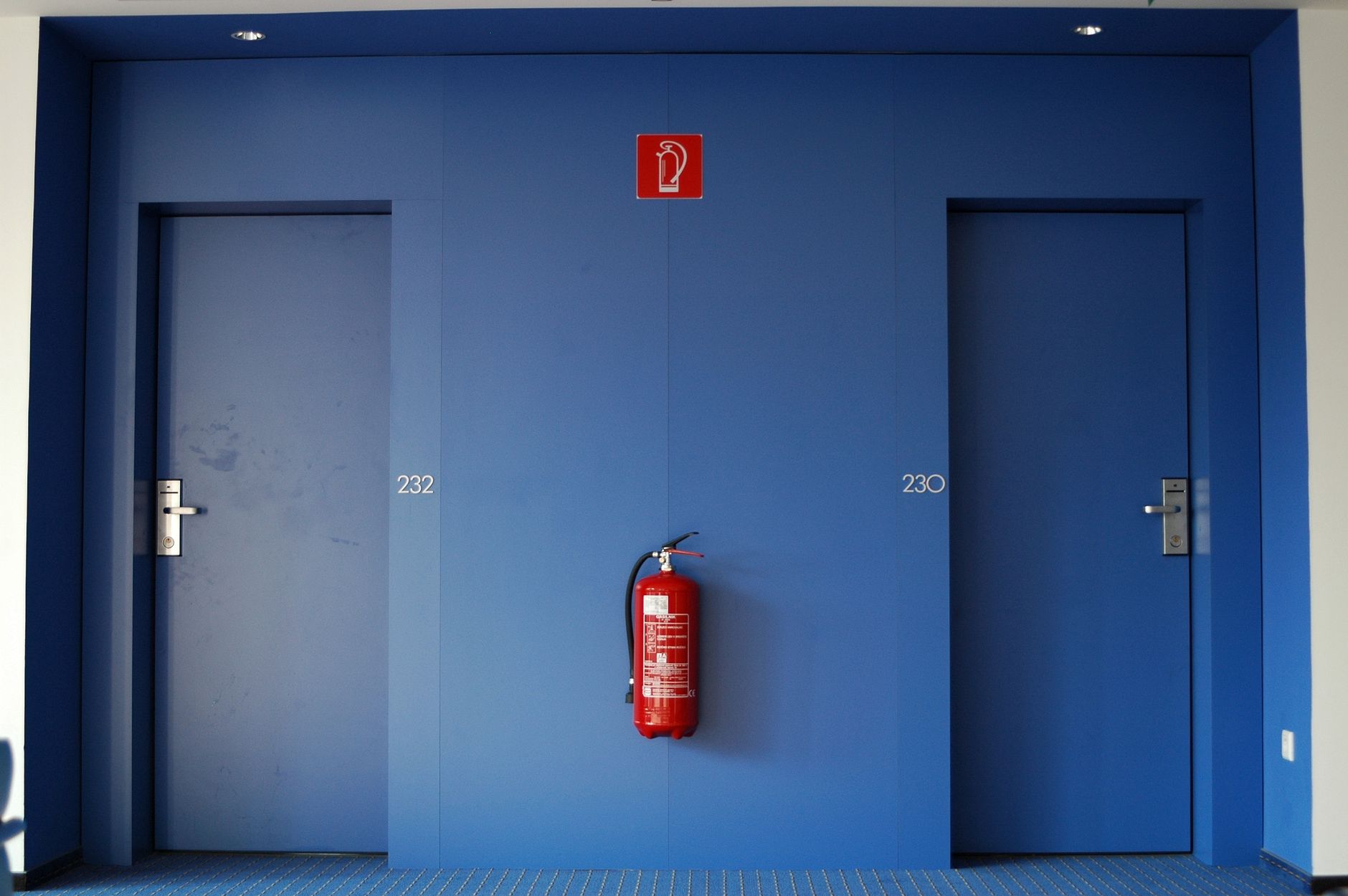 Blue doors in a corridor with a red fire extinguisher between them.
