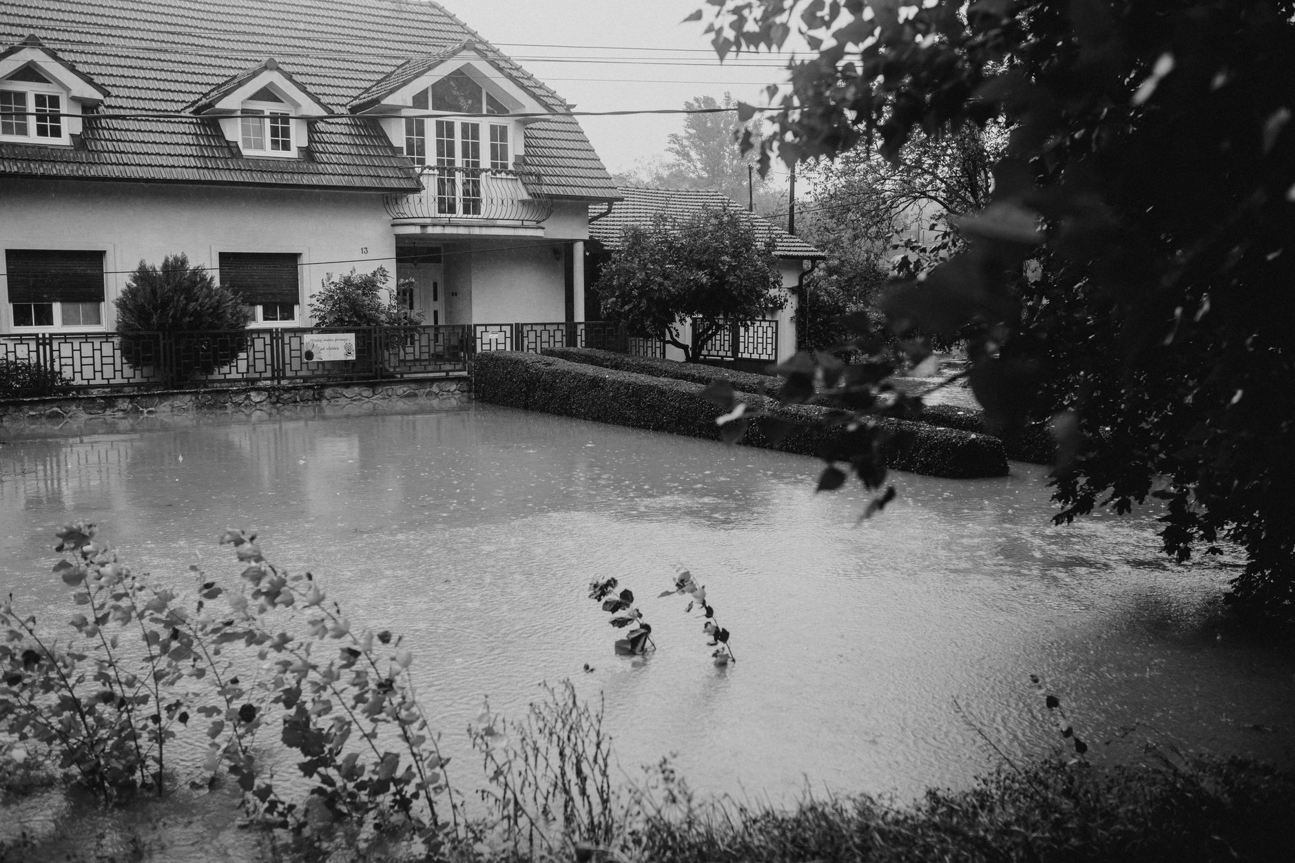 Black and white image of a suburban house affected by flooding during heavy rain.