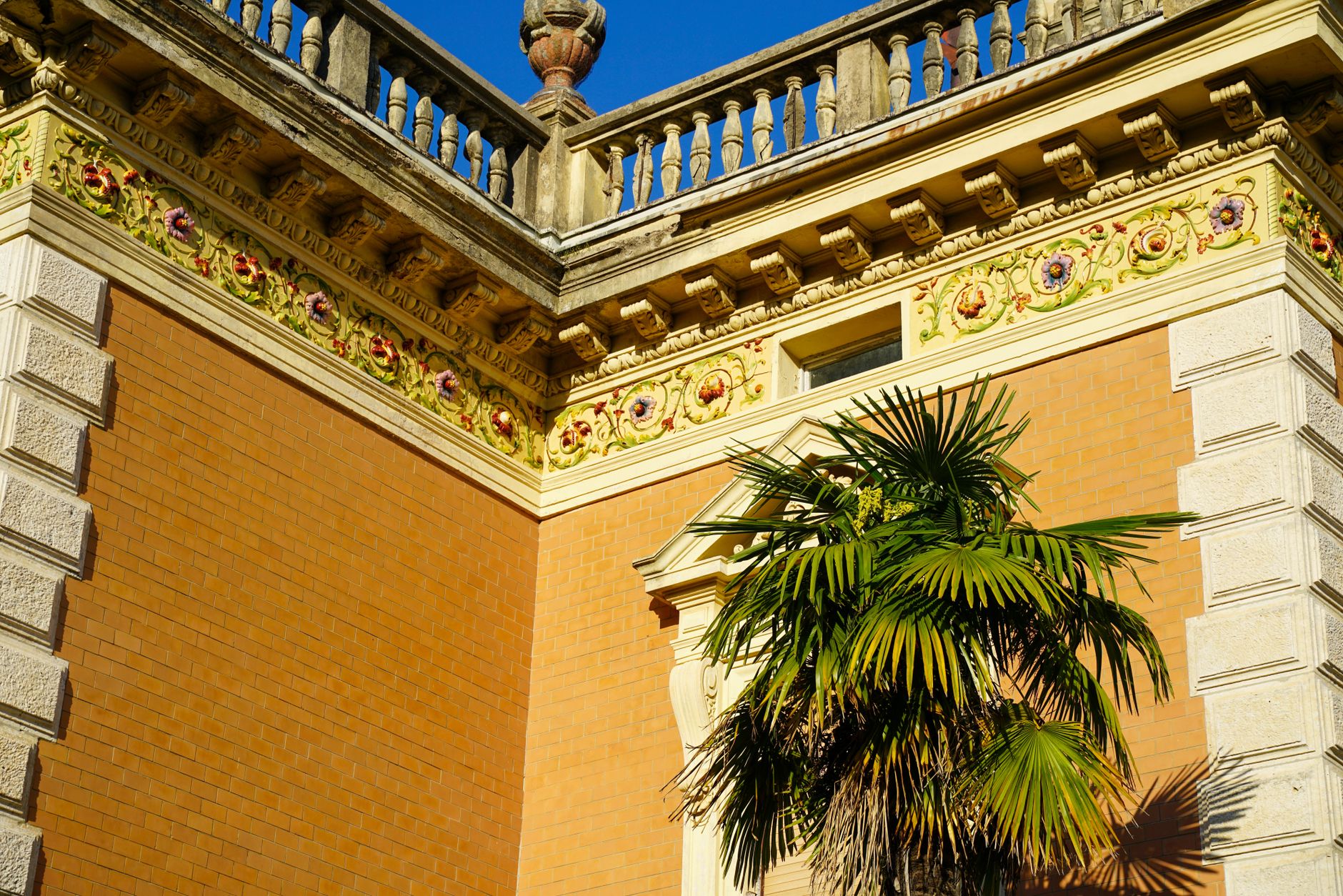 Decorative brick building facade with palm tree in Ičići, Croatia, under a clear blue sky.