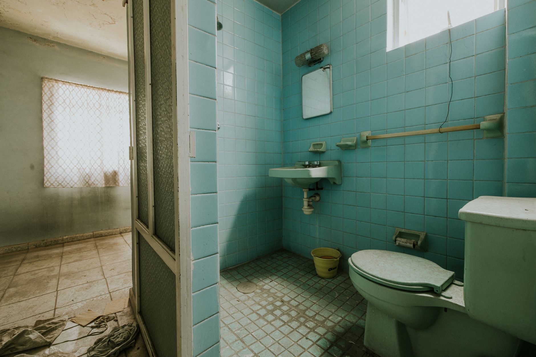 An abandoned bathroom with blue tiles, old fixtures, and a worn-out look.