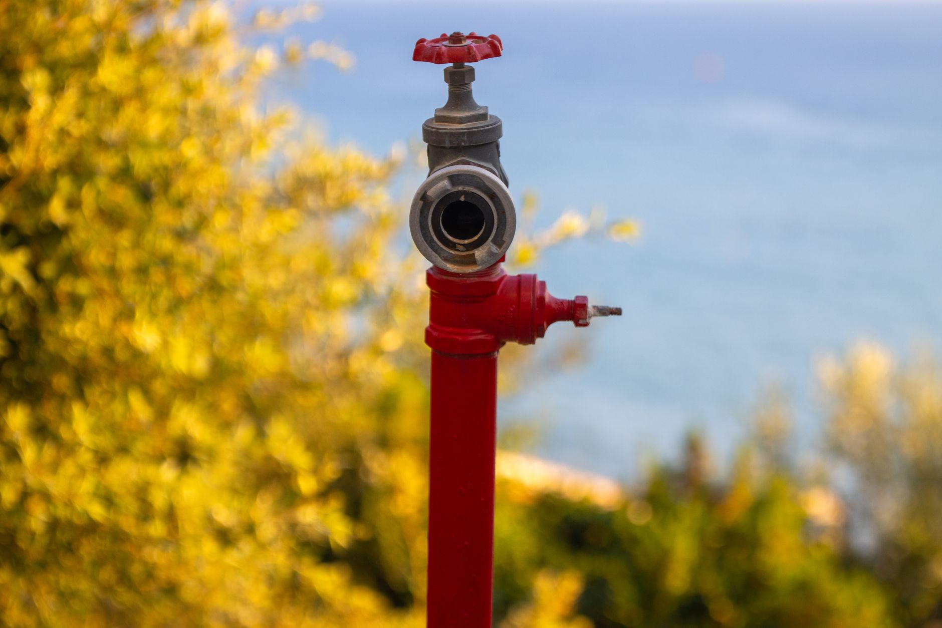 Close-up of a red valve with a sea and natural backdrop in Greece.