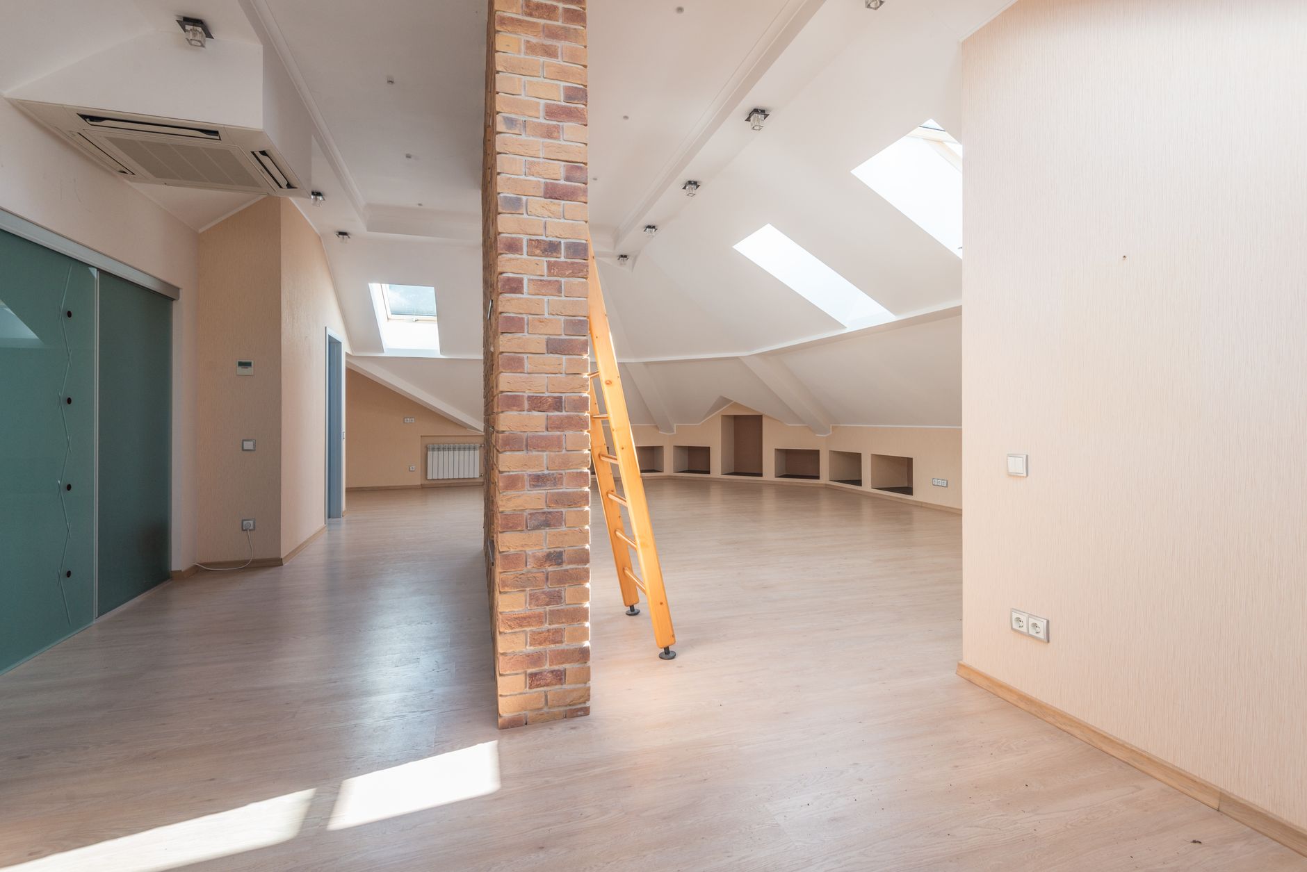 Spacious attic room with natural light from skylights, featuring a brick pillar and a wooden ladder.
