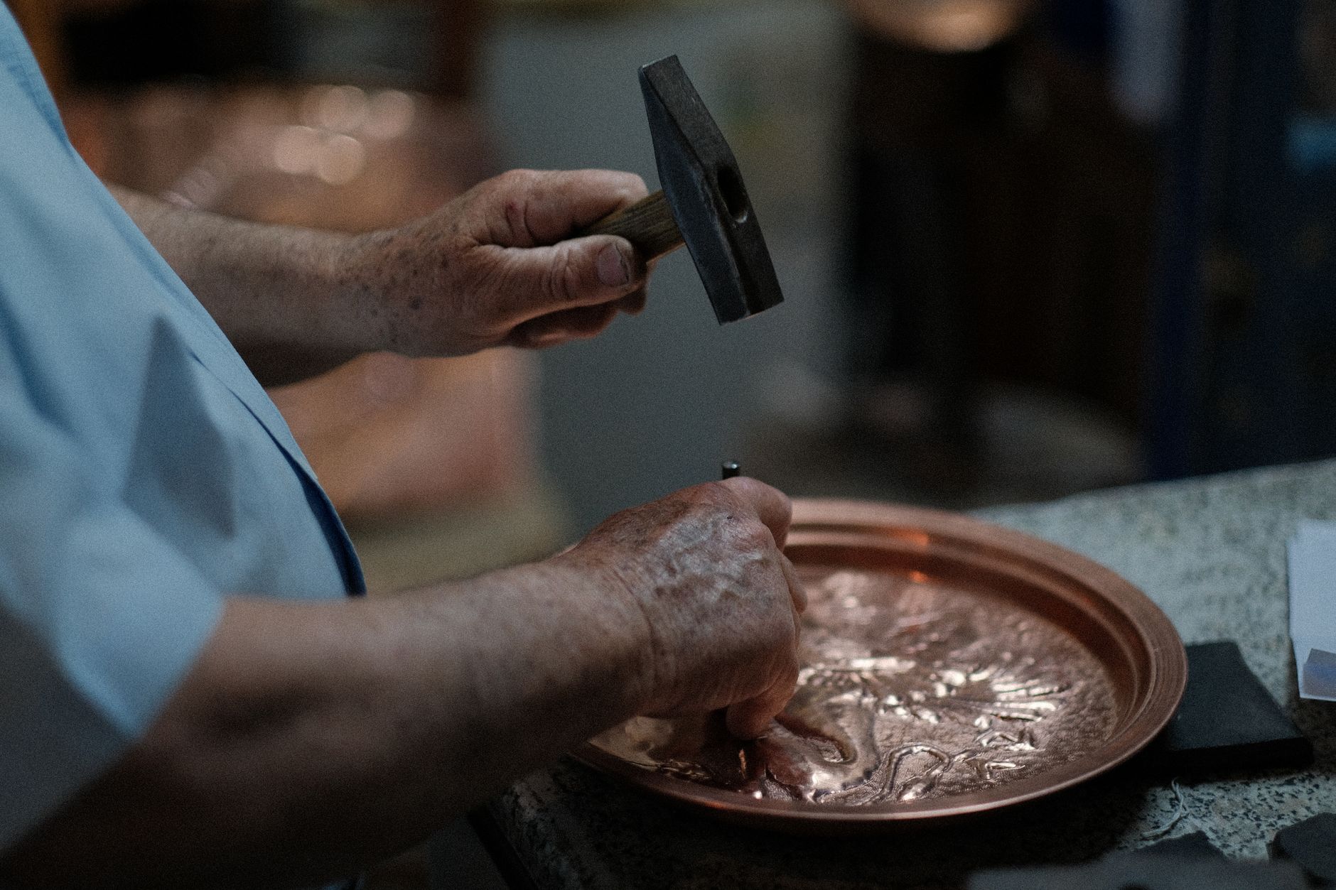Close-up of skilled craftsman hand-hammering designs into a copper plate, showcasing traditional craftsmanship.