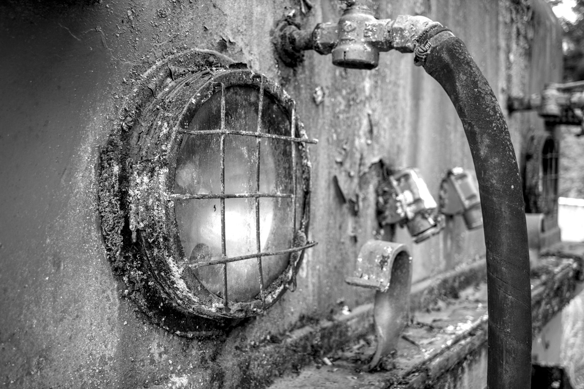 Close-up of a rusty industrial pipe and light fixture, highlighting decay and texture.