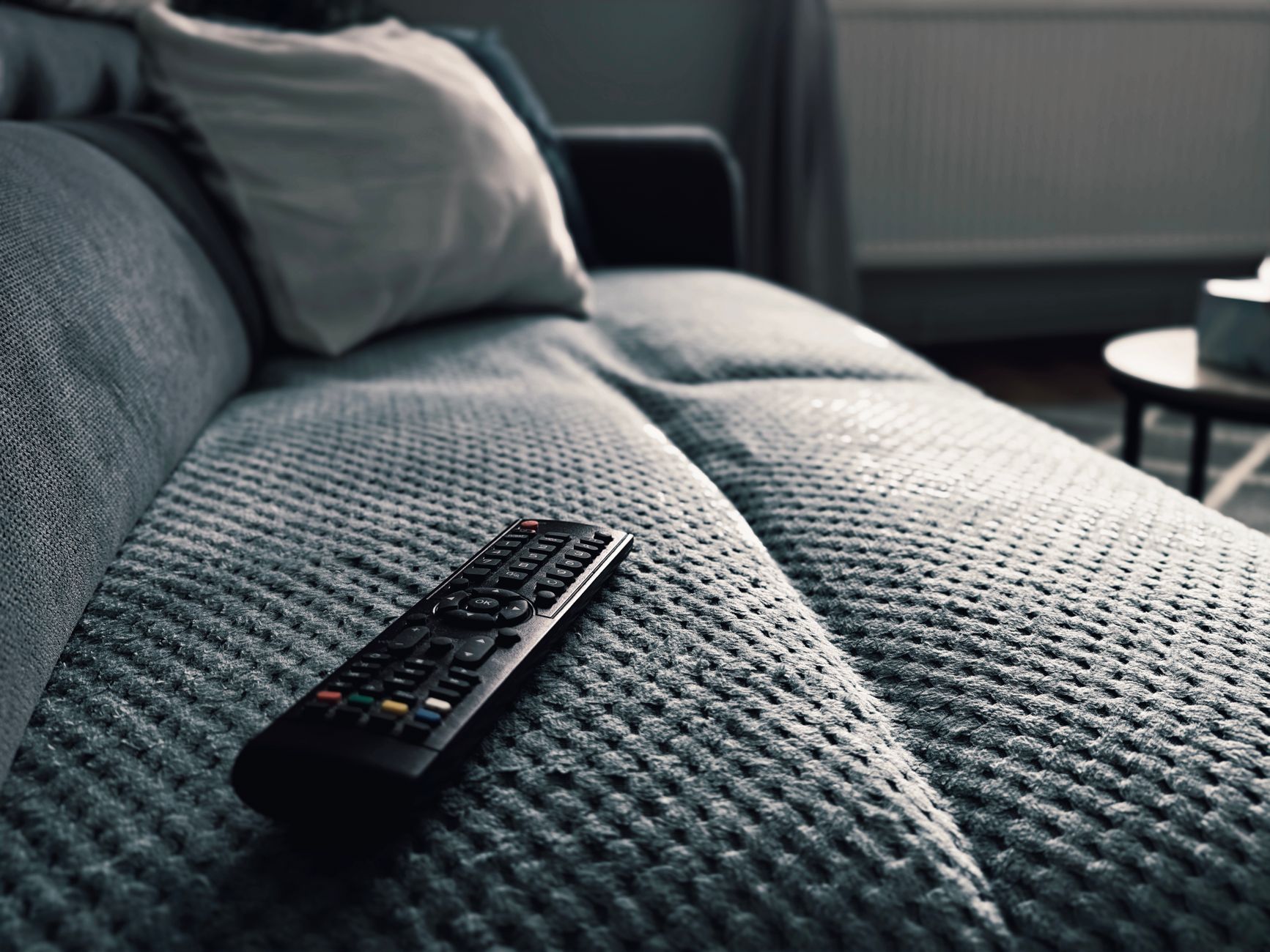A close-up of a TV remote on a textured sofa in a cozy living room setting.