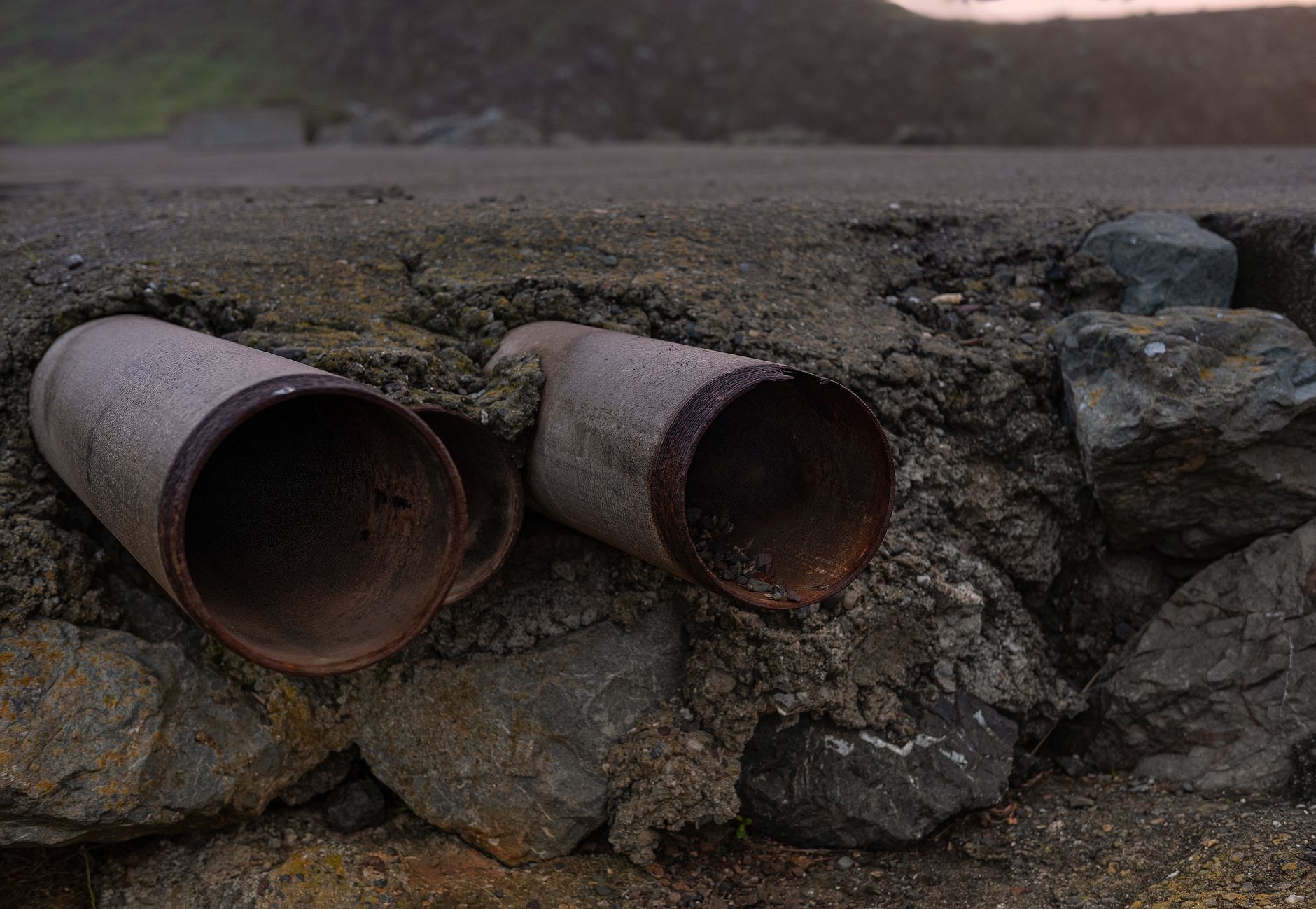 Close-up of two rusty steel pipes protruding from a rocky surface, showcasing erosion and weathering effects.