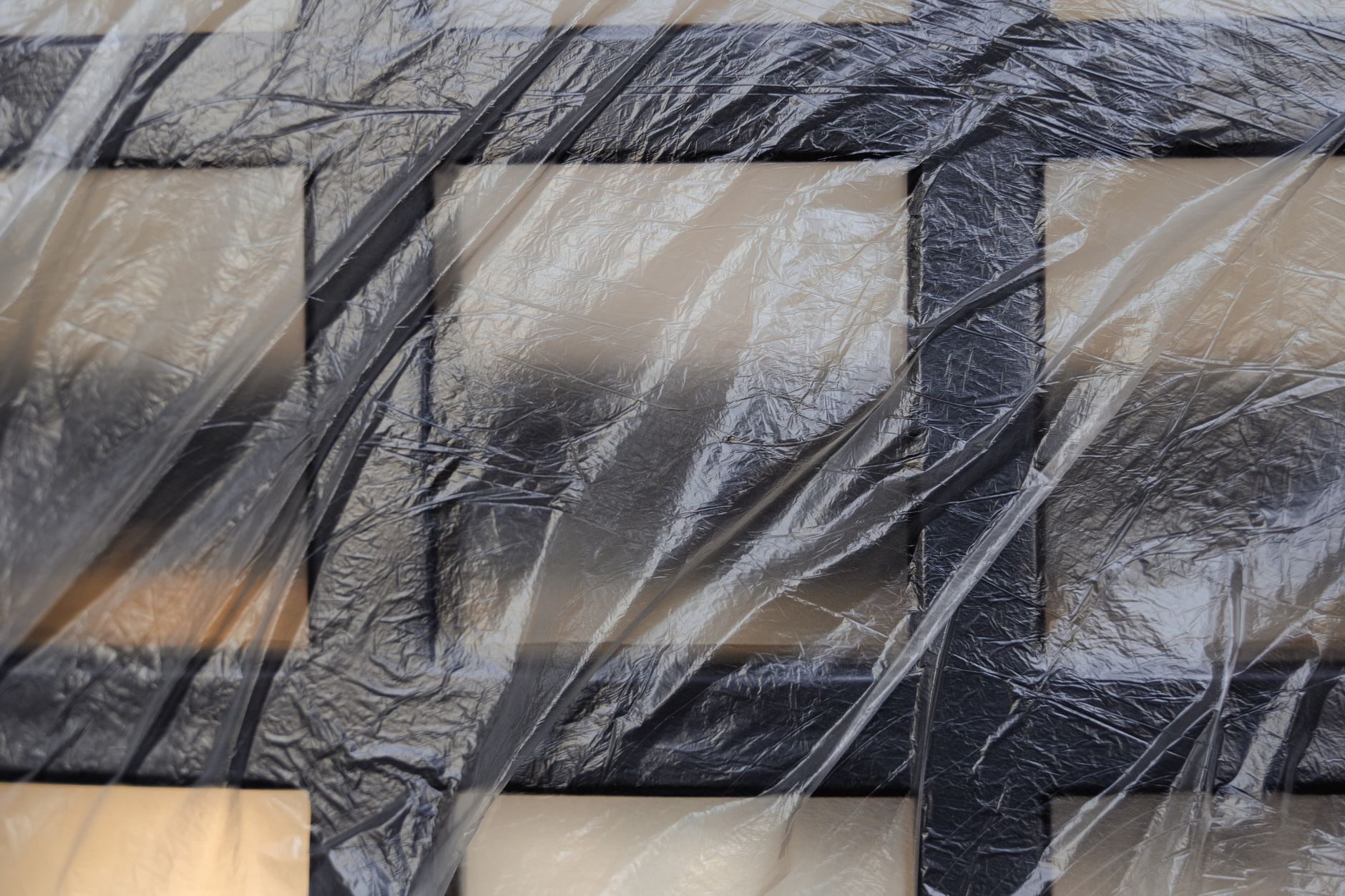 Detailed view of a plastic-wrapped black metal grid, highlighting texture and abstract pattern.