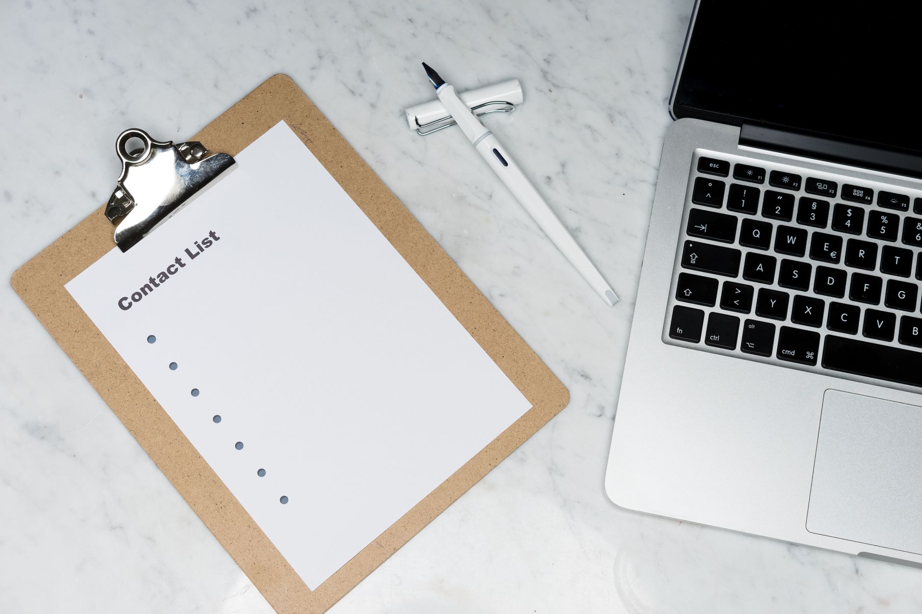 Modern office desk setup featuring a laptop, clipboard, and pen on a marble surface.