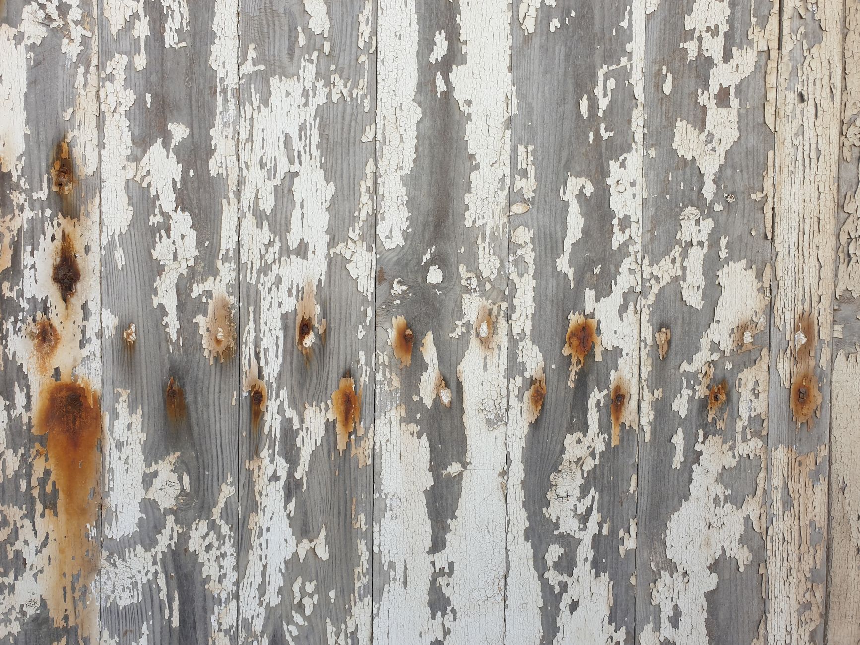 Detailed view of a rustic, worn wooden wall with peeling paint and rust patches.