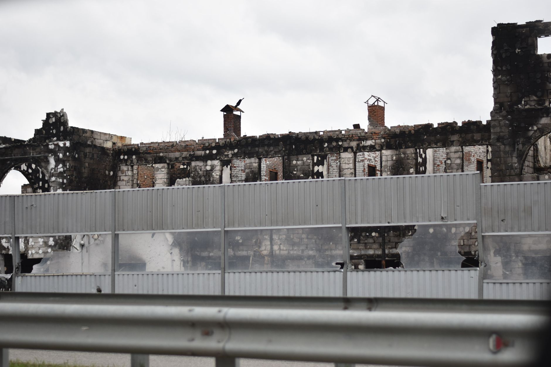 A destroyed building behind a metal noise barrier, hinting at past conflict.