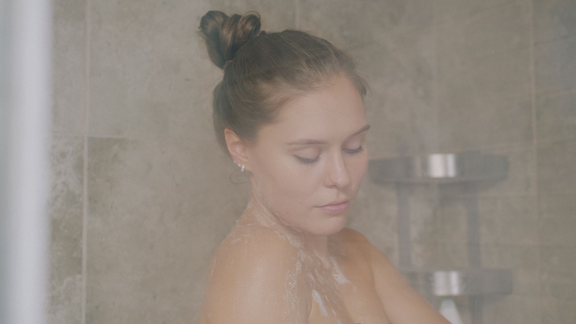 A serene woman bathing in a shower with soft lighting and steam.