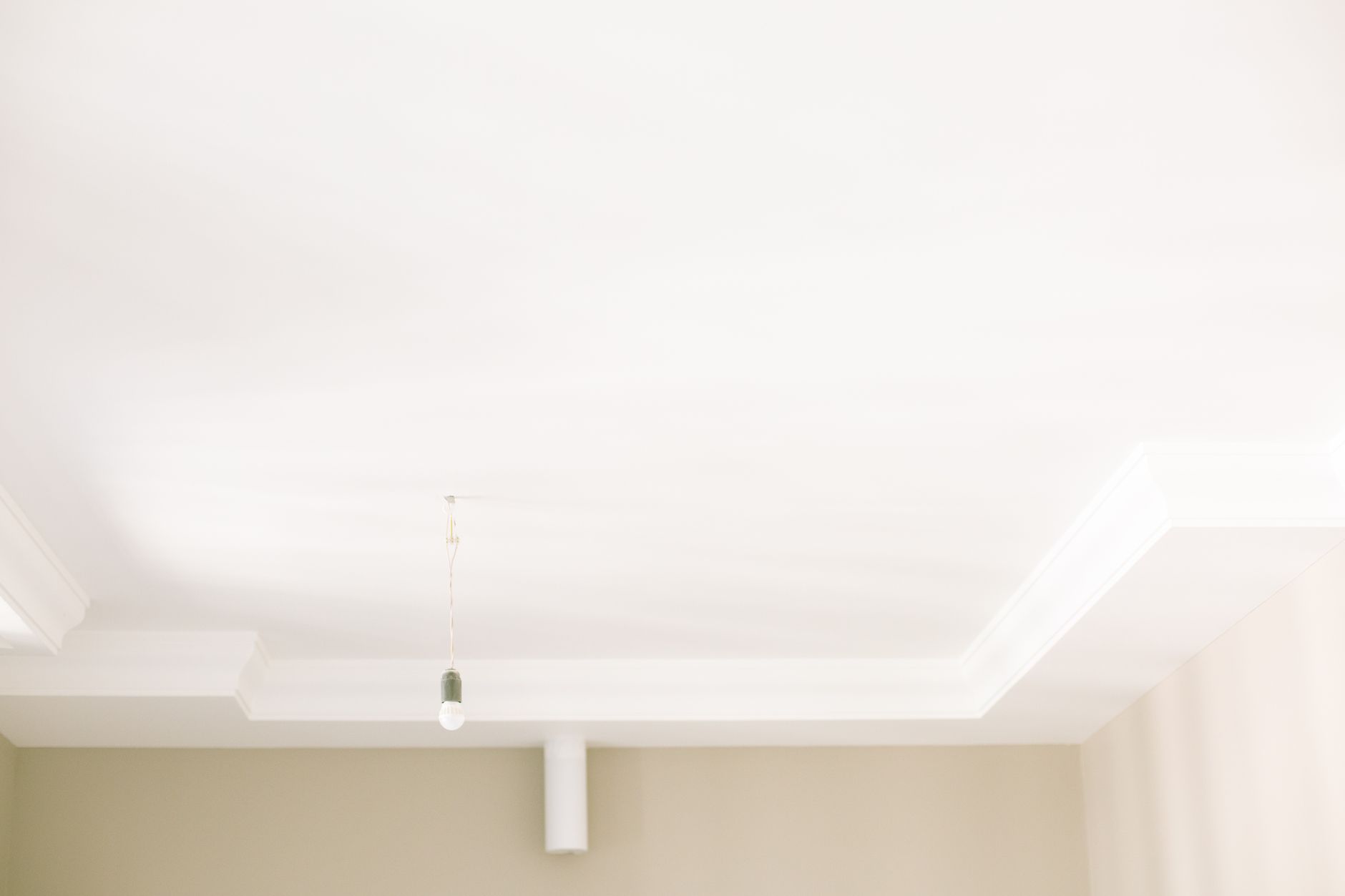 Bright white ceiling with a single hanging light bulb highlighting minimal interior design.