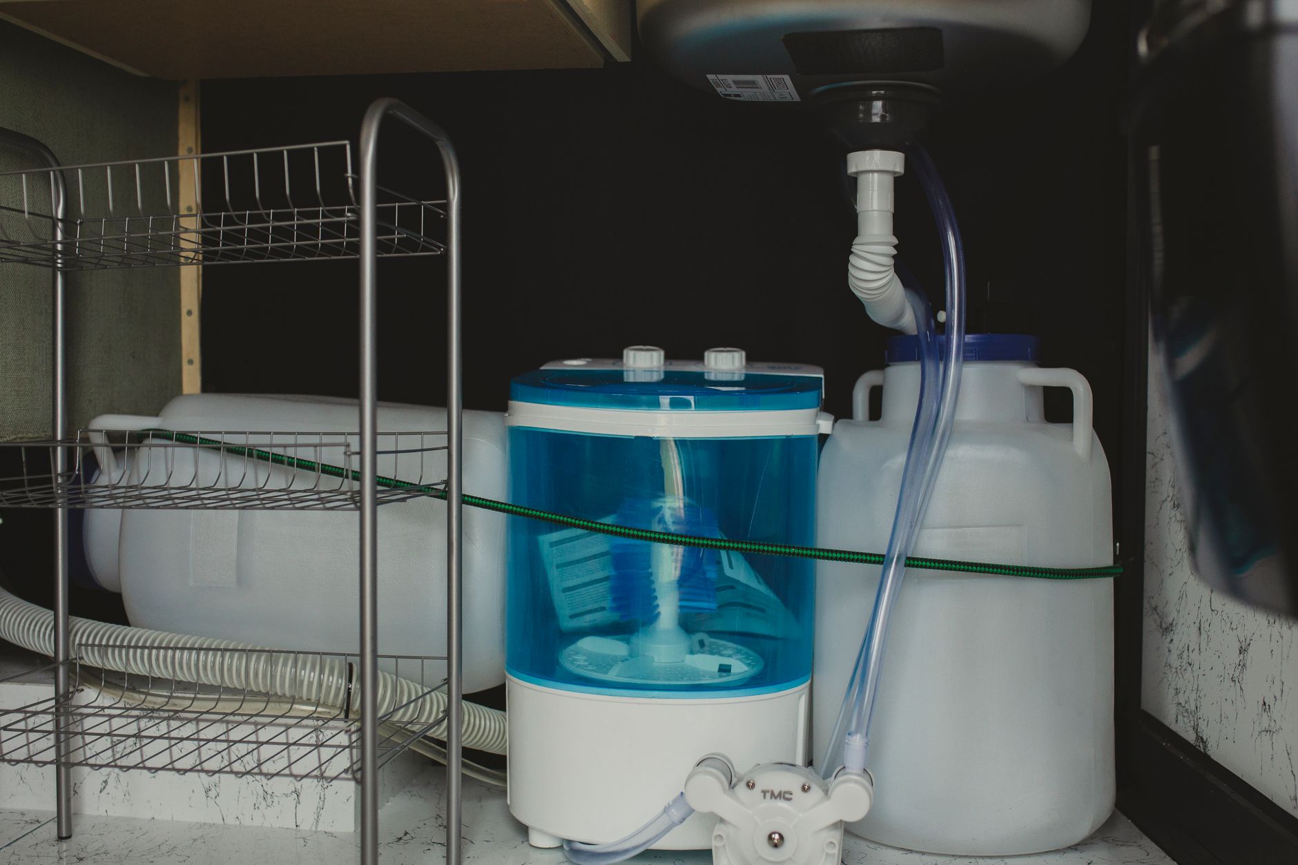 Compact travel-size washer in a storage area with plastic containers and tubing system.