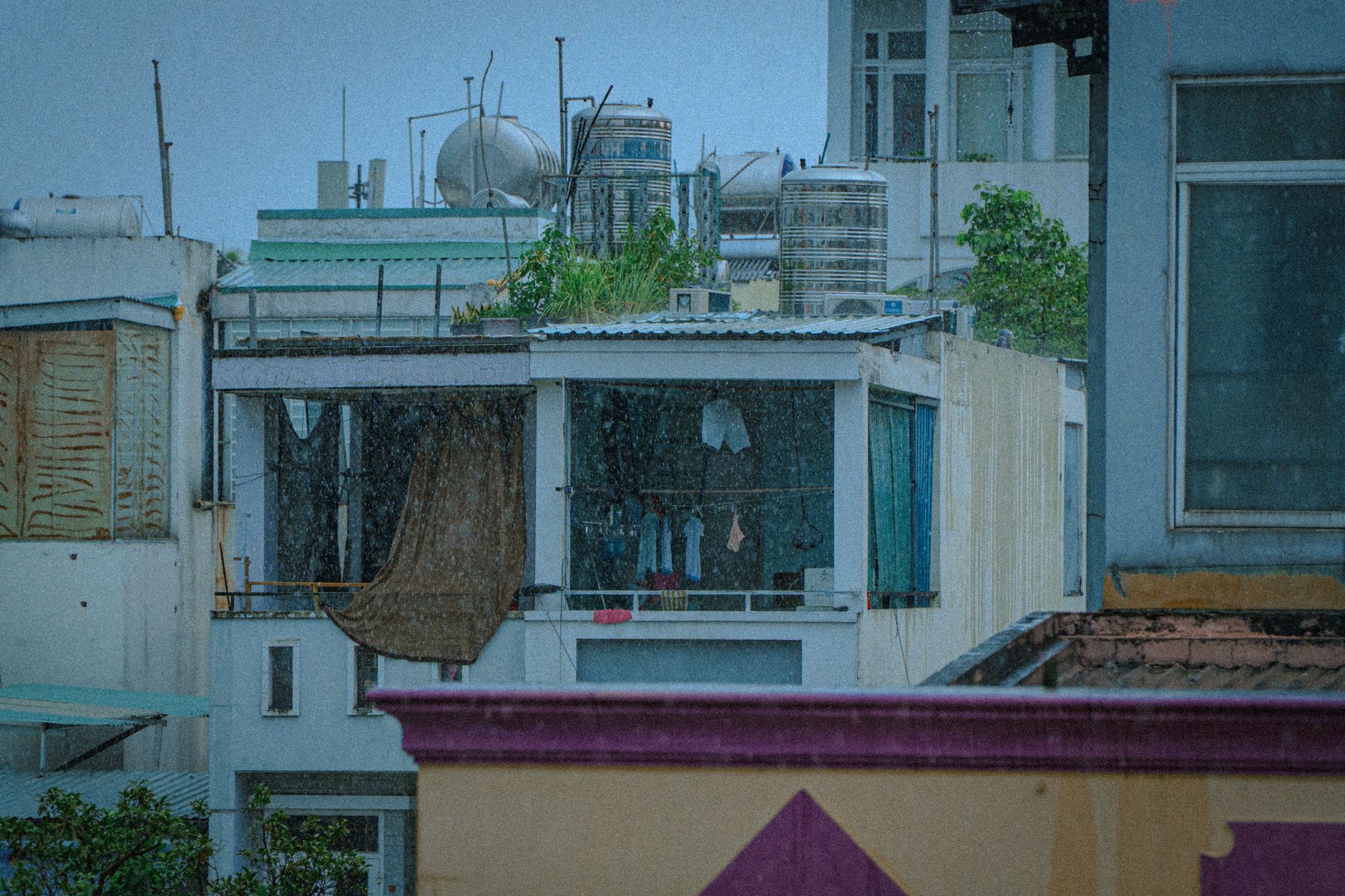 Urban rooftops in rain with water tanks and drying laundry, showcasing rainy day mood.