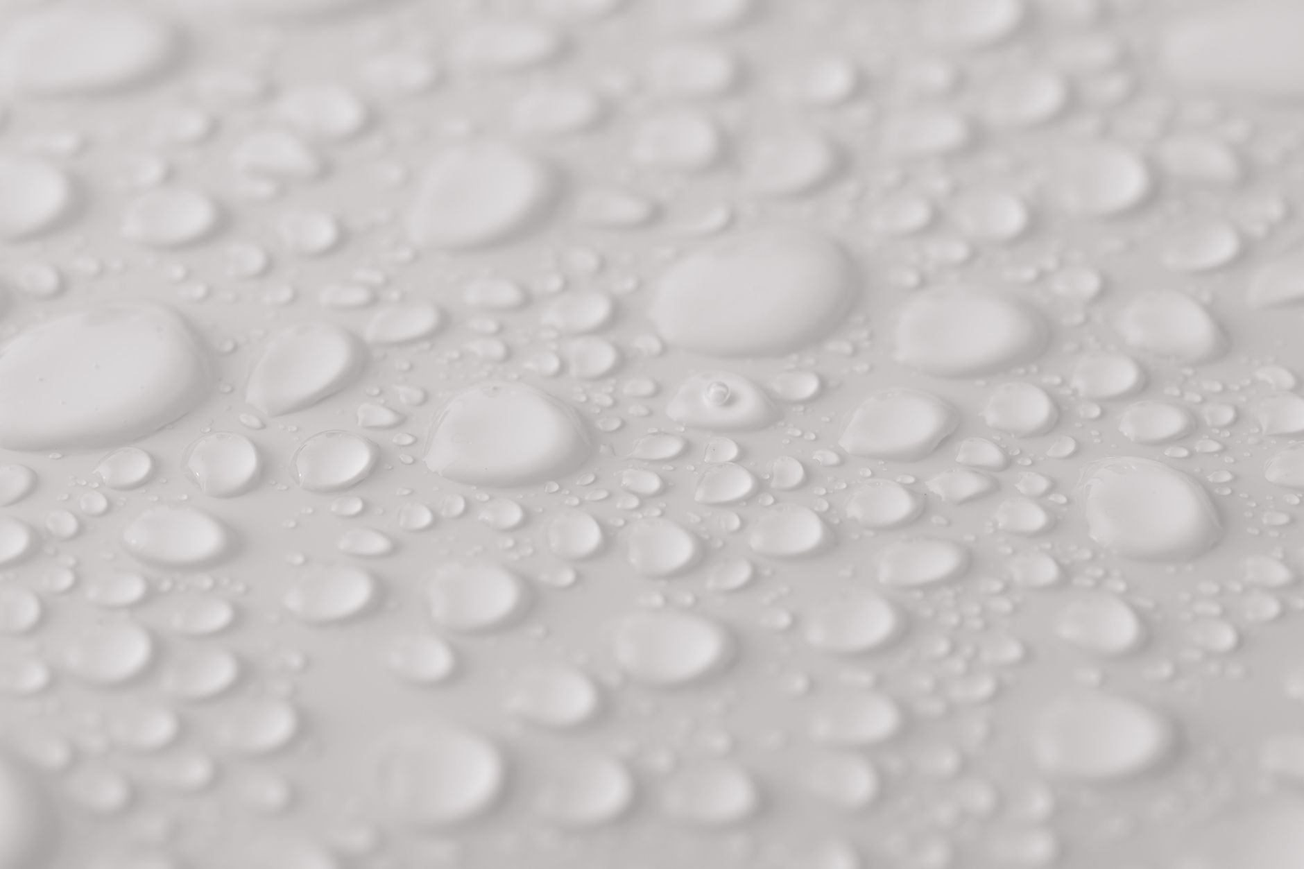 Closeup from above of clean white background with transparent glassy water drops of different sizes and shapes with blurred sides