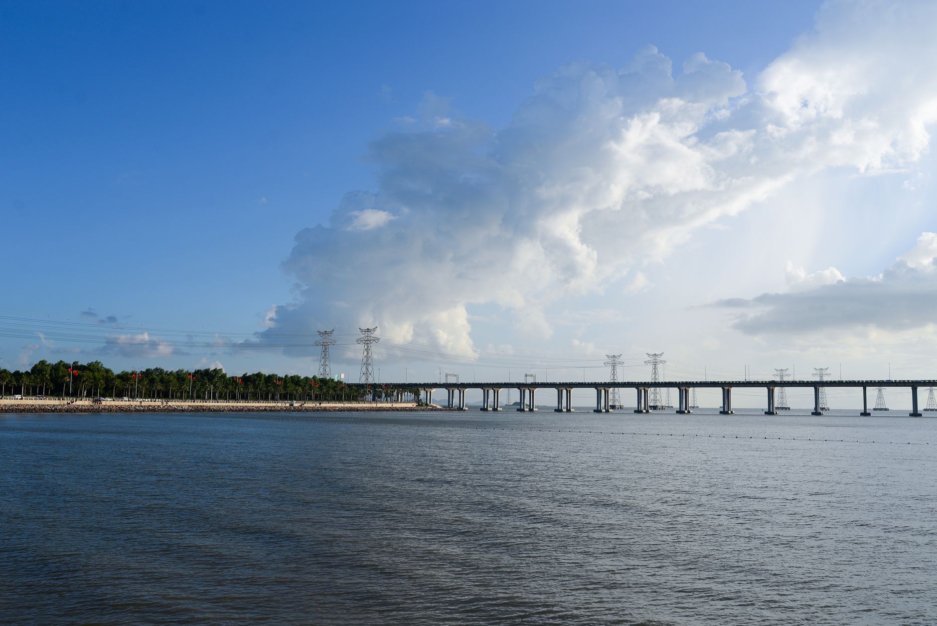 Peaceful river scene with a long bridge under a blue sky and scattered clouds.