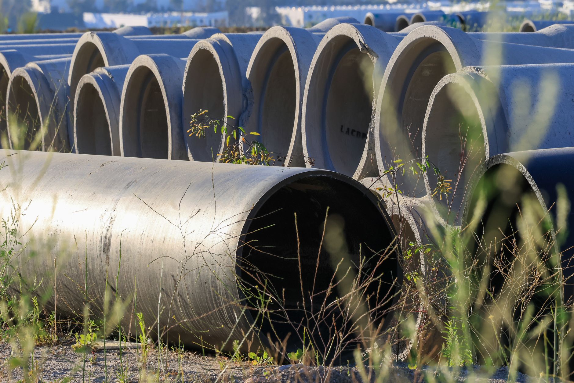 Stacked concrete pipes in an outdoor storage area surrounded by grass.